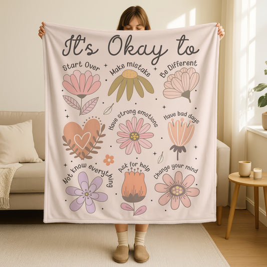 It's Okay mental health affirmation blanket in soft cream with pastel flowers and encouraging phrases including start over, make mistakes, be different, have strong emotions, have bad days, ask for help, change your mind, and you don't know everything