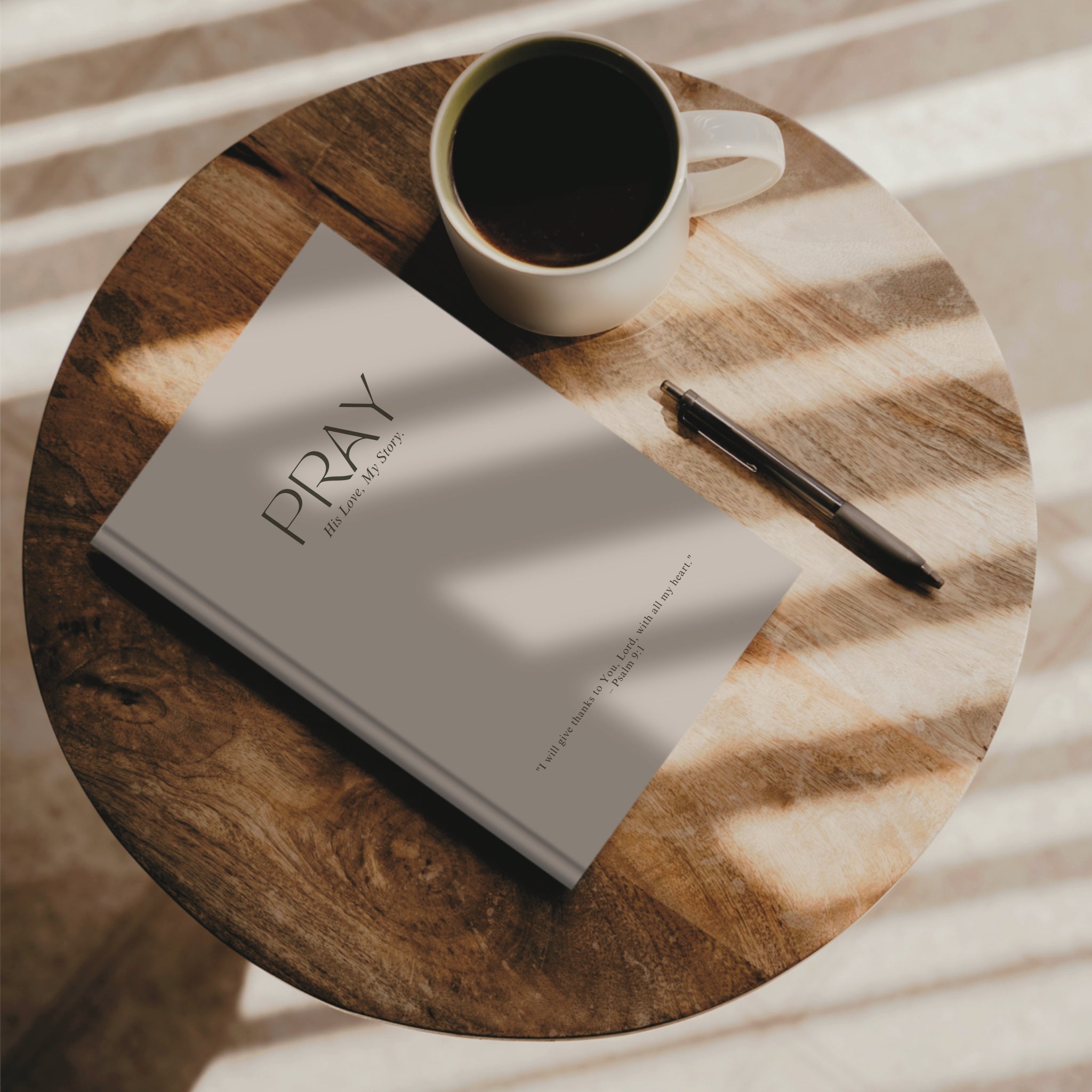 Soft stone beige faith journal resting on wooden surface next to a coffee and a pen.
