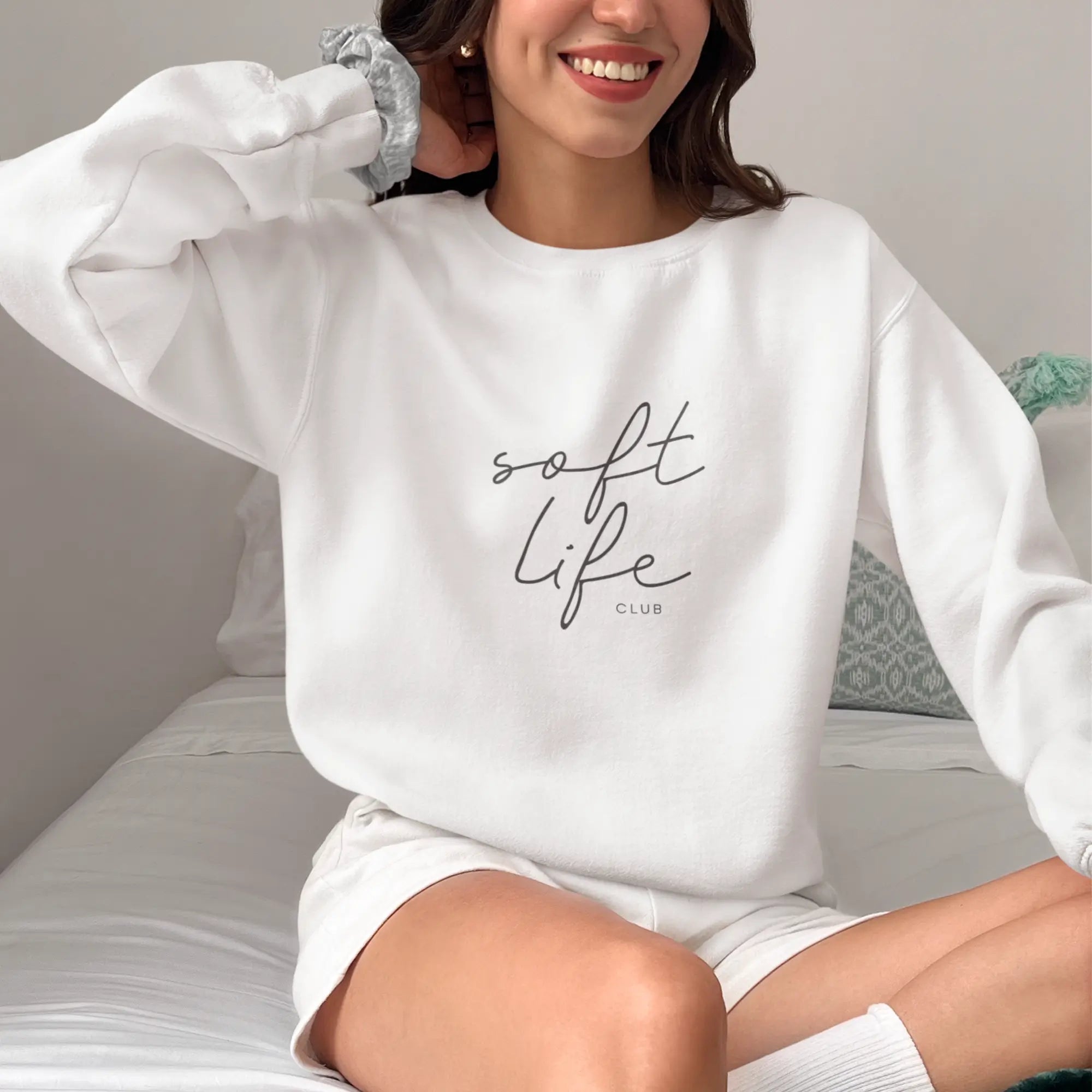 Woman wearing white 'Soft Life Club' sweatshirt, premium cotton-blend loungewear for comfort seekers