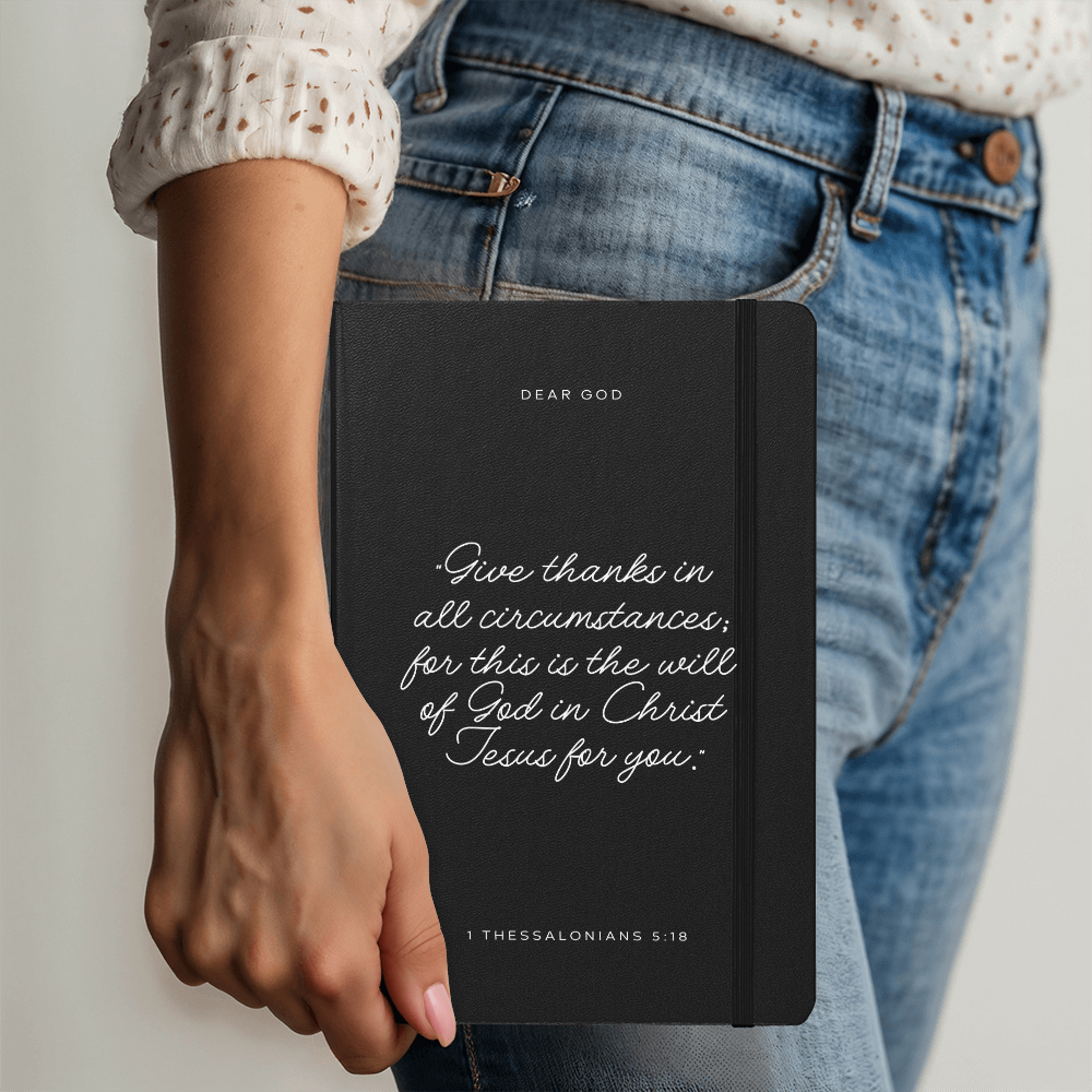 Black prayer journal with a bible quote on the front and 'dear God' being held in a woman's hand.