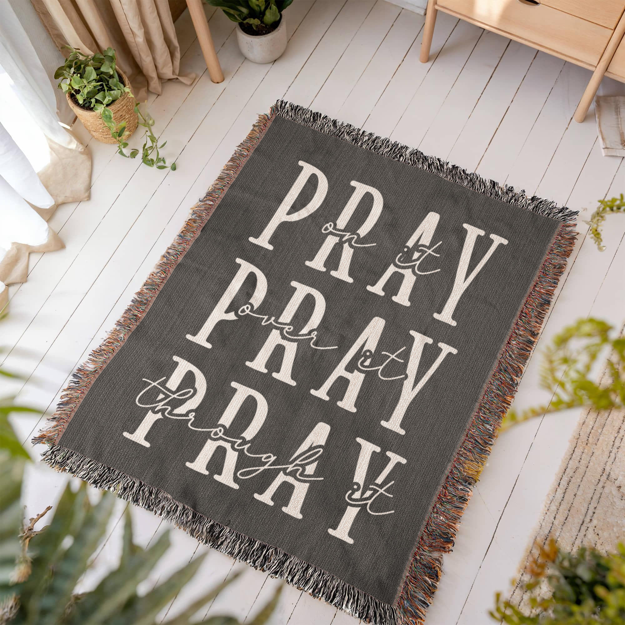 A beautifully textured cotton blanket with an embroidered faith-filled quote, laying flat on a floor.