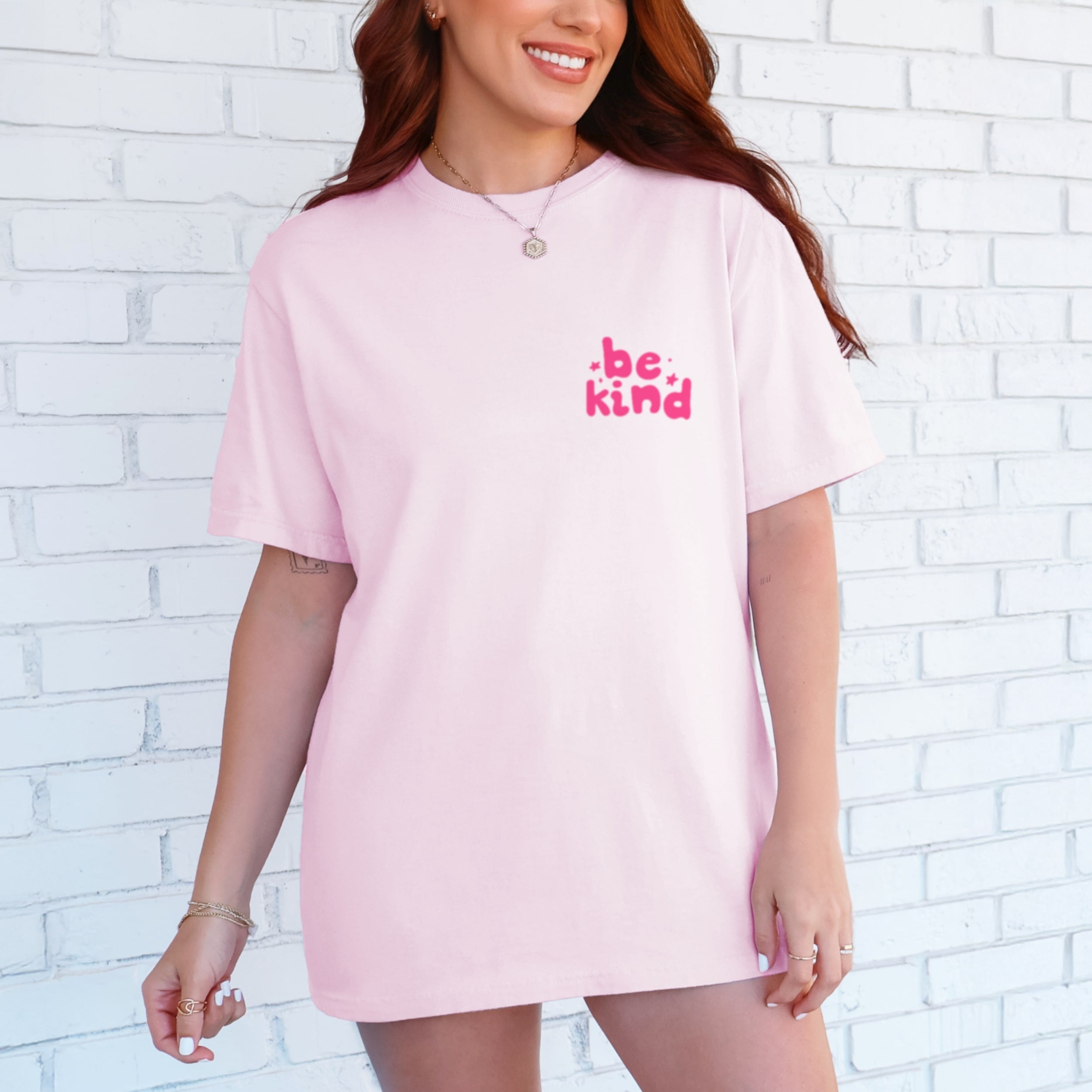 Woman wearing light pink Be Kind tshirt with small hot pink text on front chest, blossom colored inspirational graphic tee