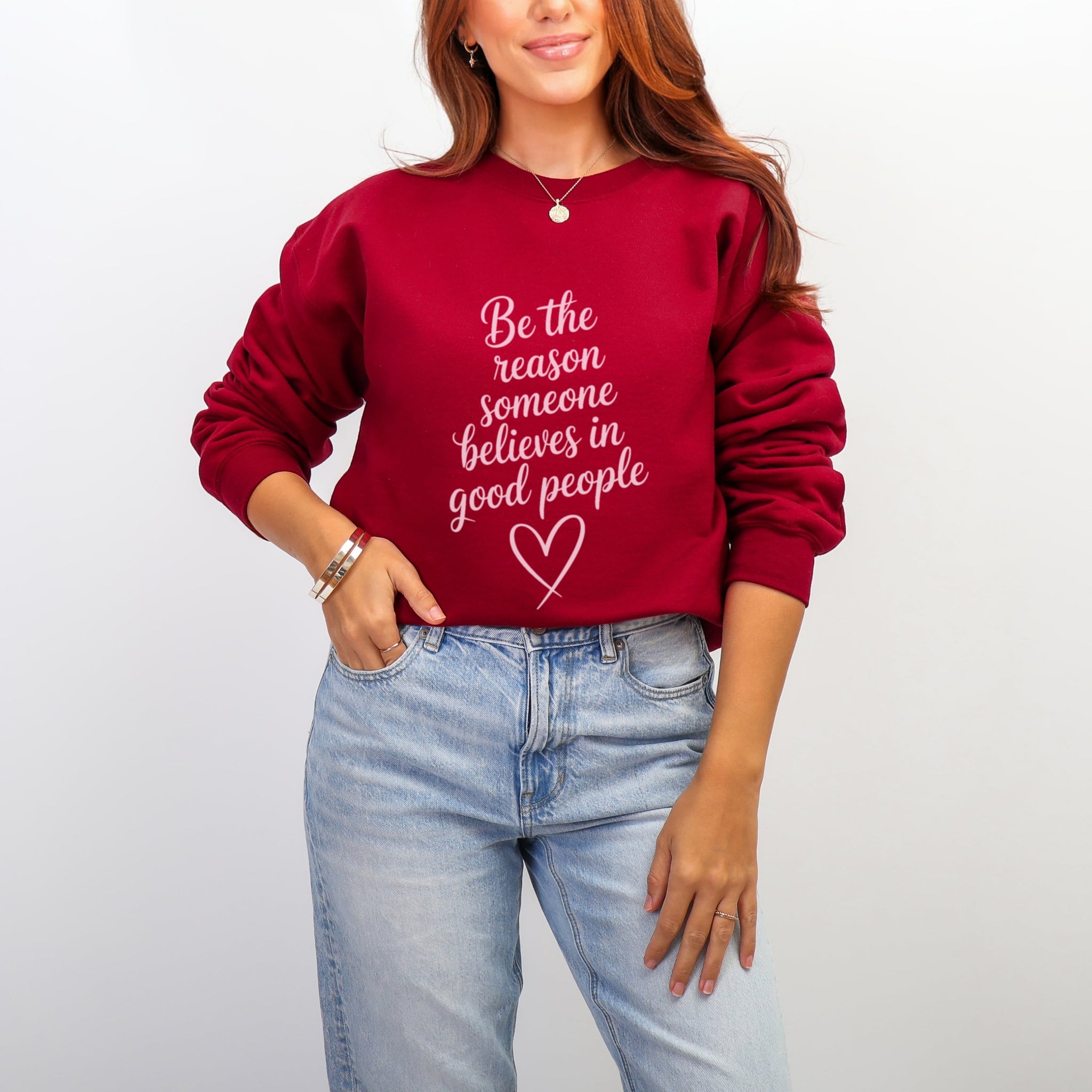 Woman wearing cardinal red Be The Reason Someone Believes In Good People sweatshirt with pale pink text - inspirational kindness crewneck for women
