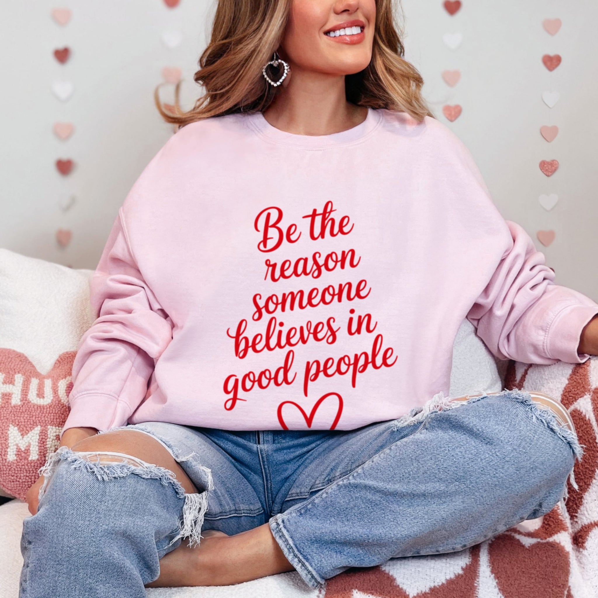 Woman wearing pink kindness crewneck that says Be The Reason Someone Believes In Good People on the front of the sweatshirt