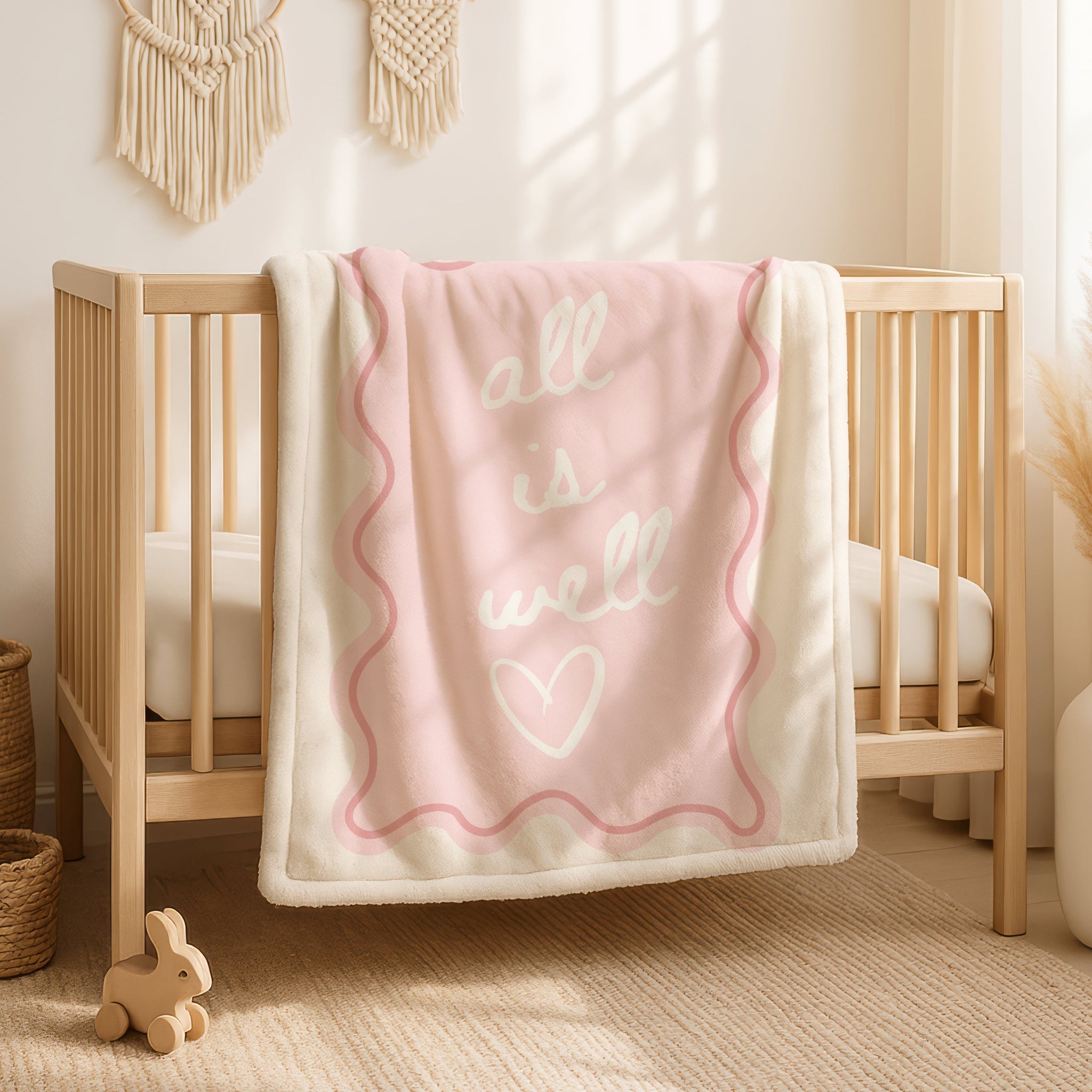 All is well blanket in soft blush pink with cream background and pink wavy scalloped border, gentle script text saying all is well with small heart, calming Christian throw blanket