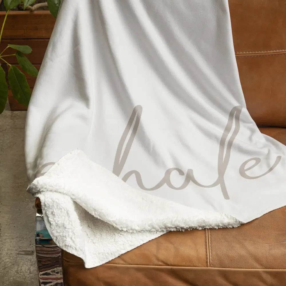 Cozy large sherpa throw blanket with the word “exhale” in script lettering drapped over a chair