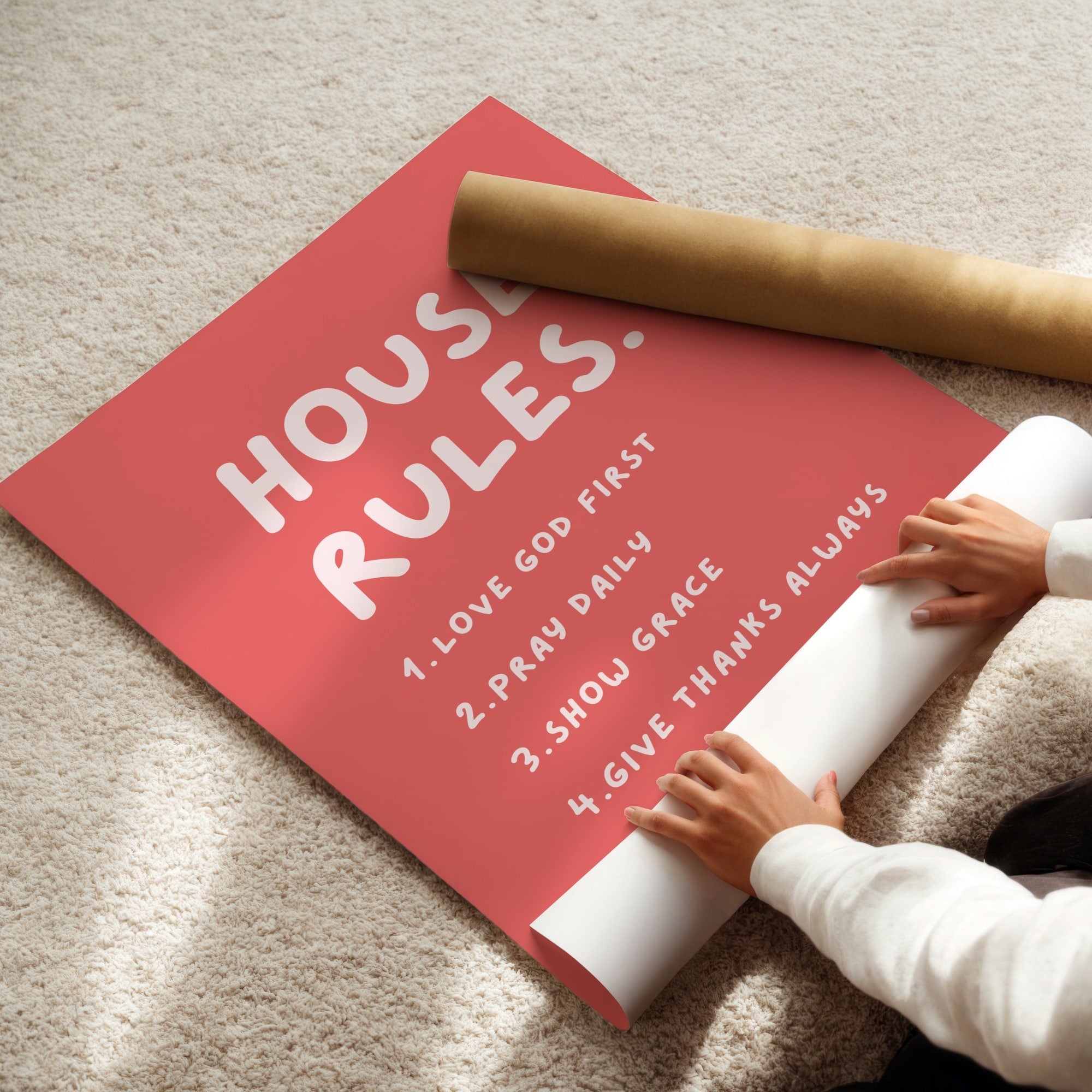 Person unrolling a poster print with 'HOUSE RULES' text on a beige carpet.
