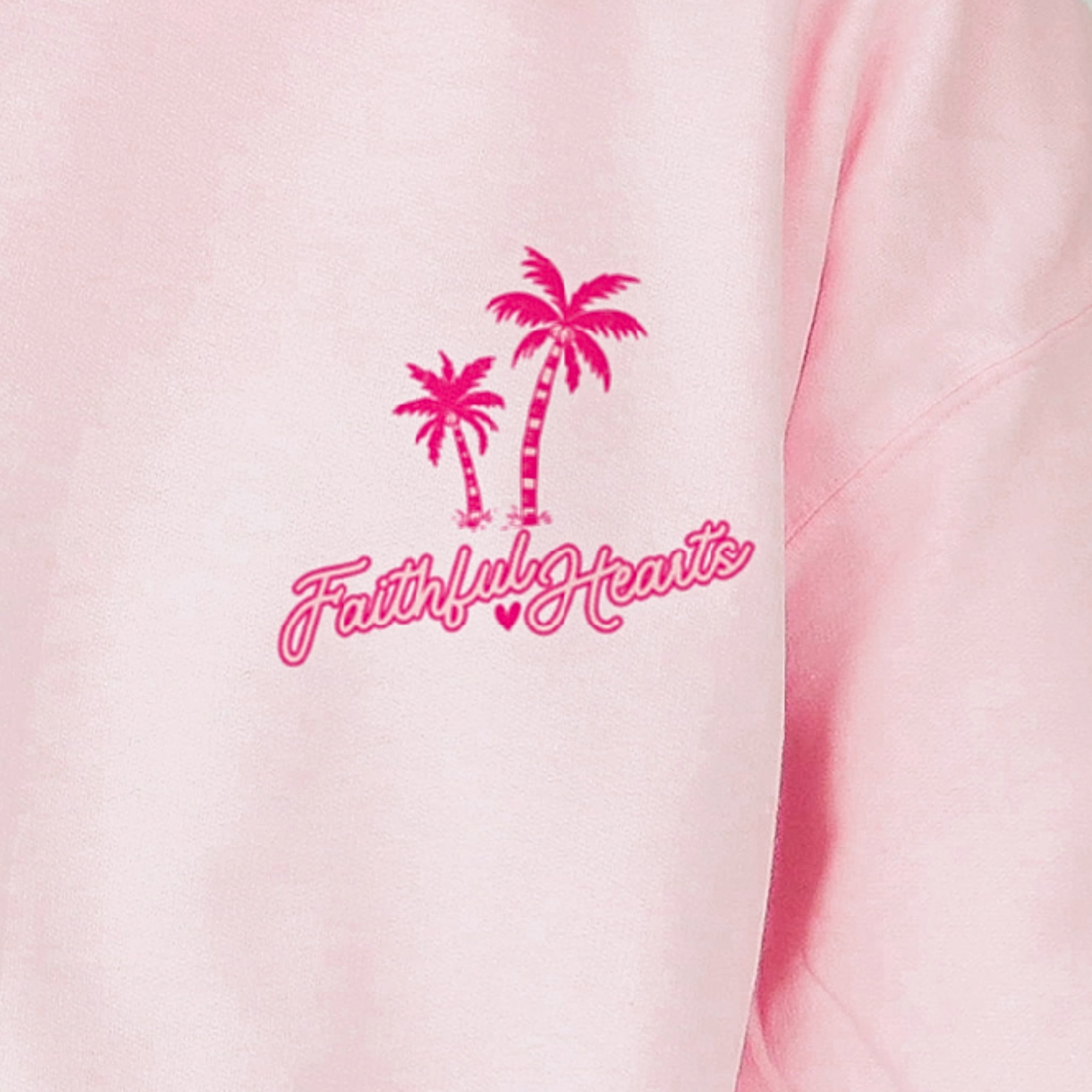 Close up of Faithful Hearts logo on pink hoodie with palm trees, faith-based clothing brand detail