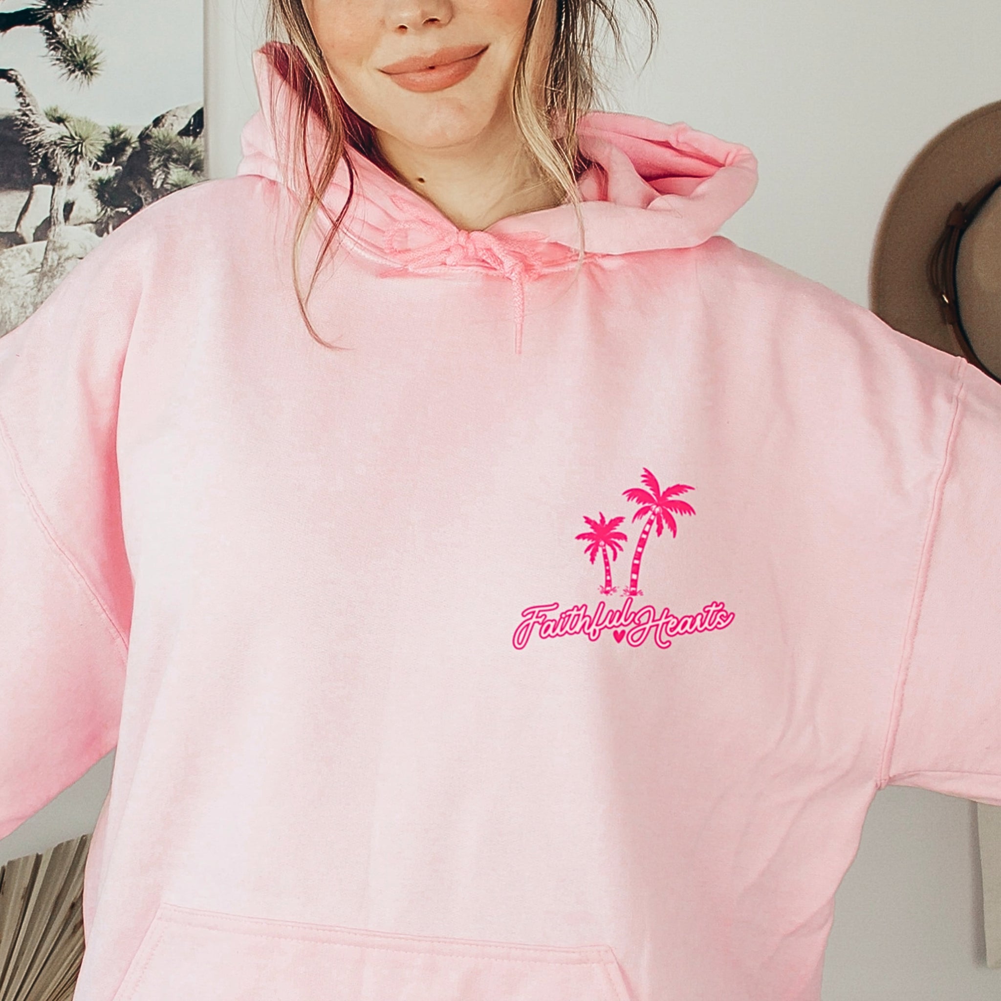 Woman wearing pink Faithful Hearts hoodie with palm tree logo, faith-based brand sweatshirt for women