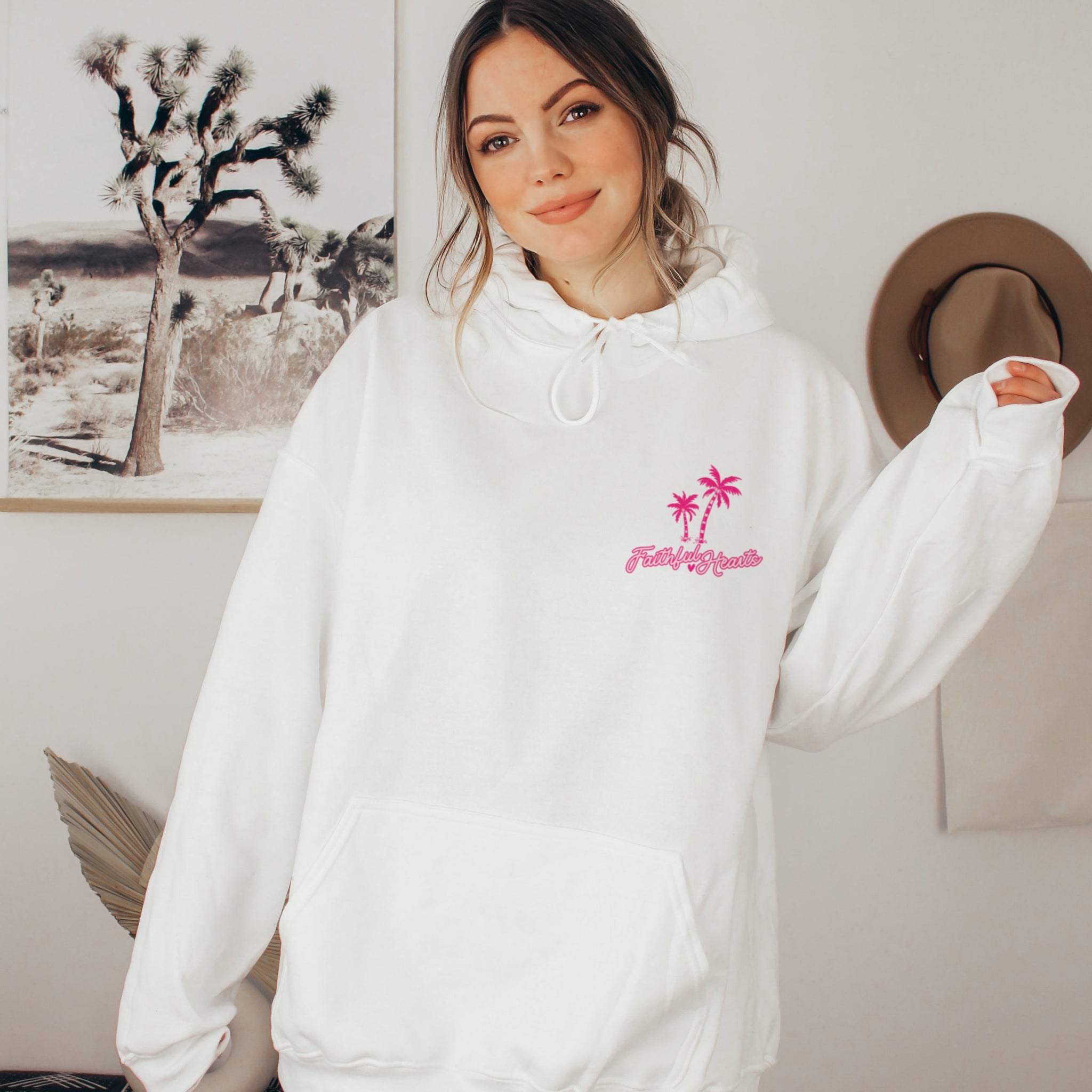 Woman in white Faithful Hearts hoodie with pink palm tree logo, cozy faith-based sweatshirt