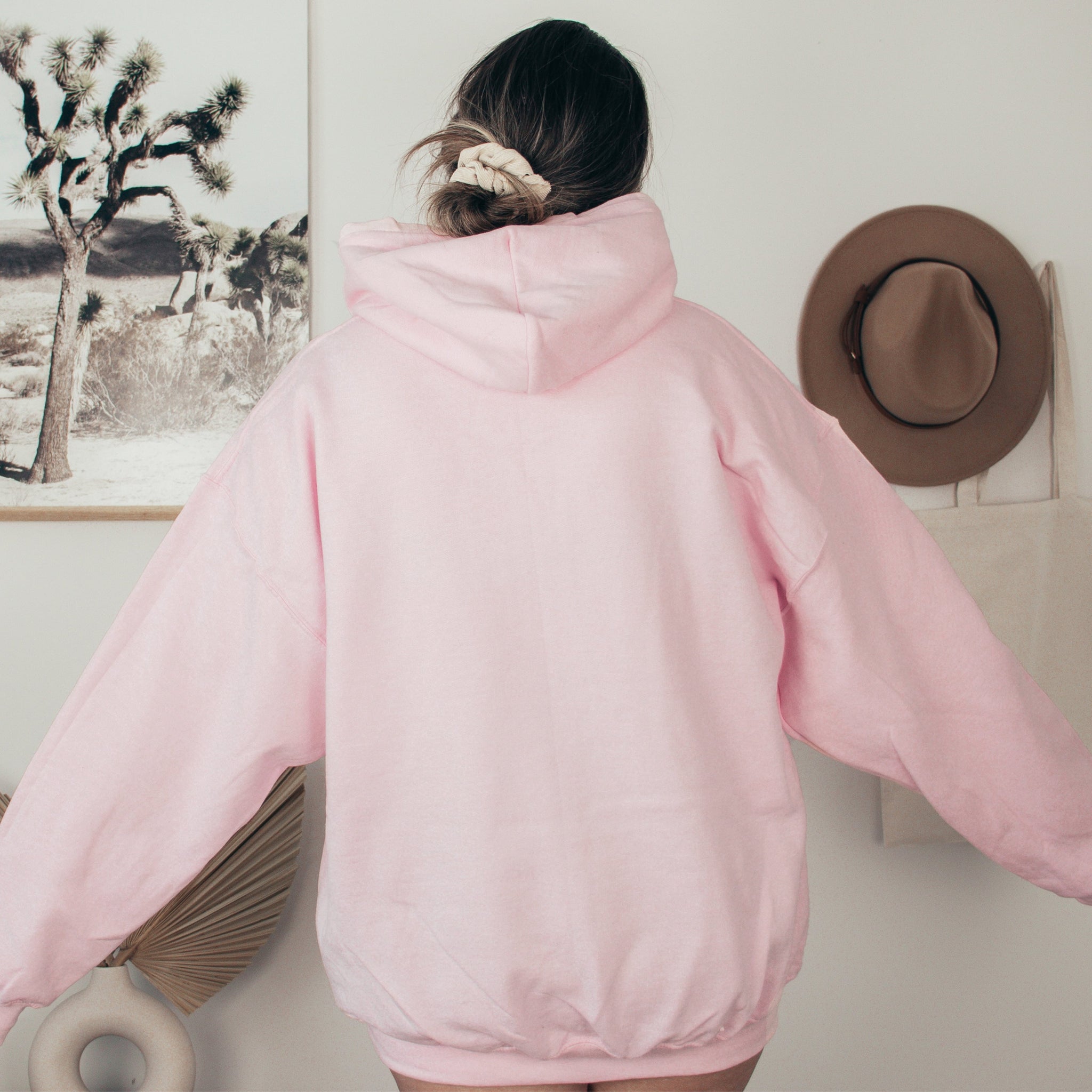Person wearing a pink hoodie with a hat and fan in the background