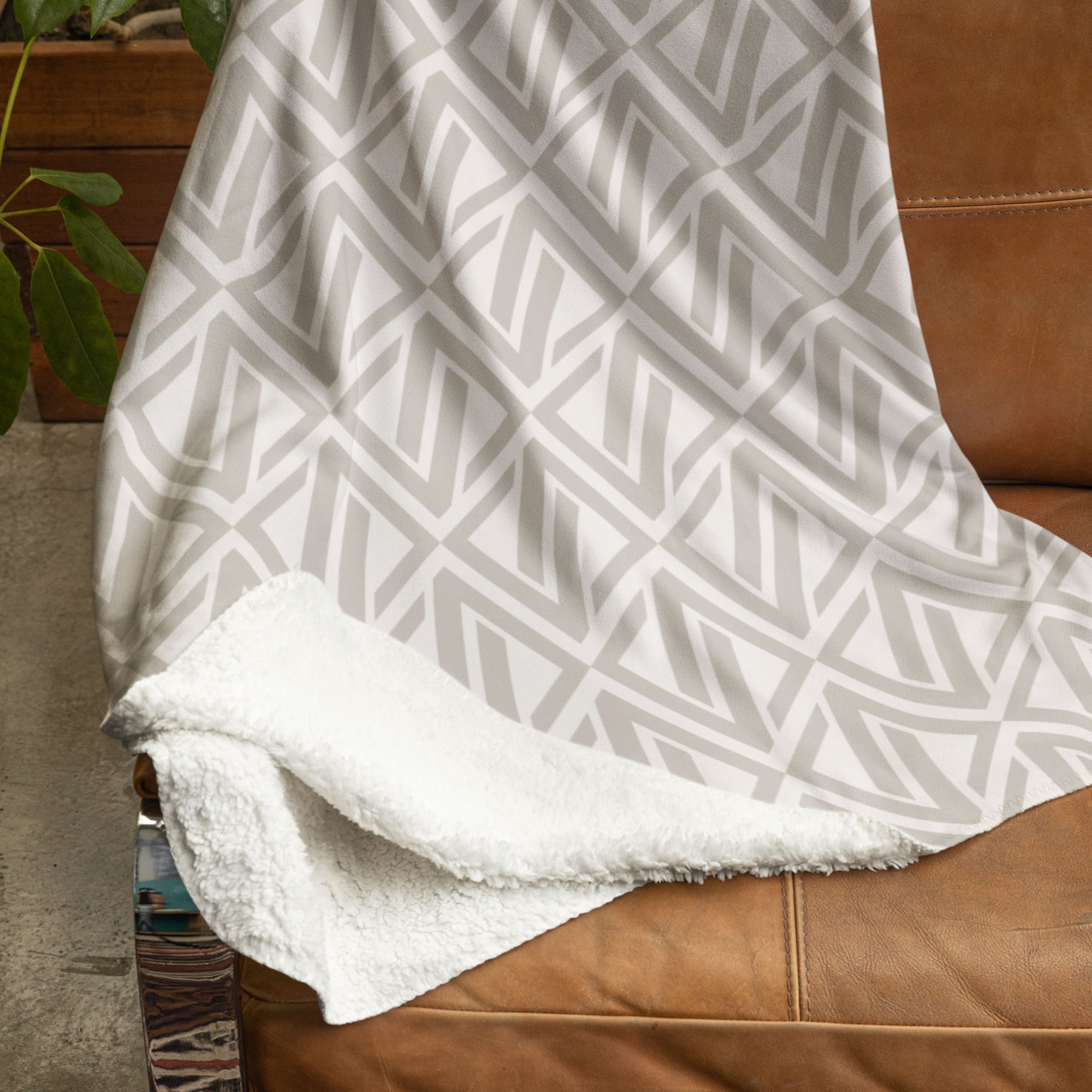 sherpa blanket with a cream geometric pattern with the faithful hearts logo laying over a leather chair