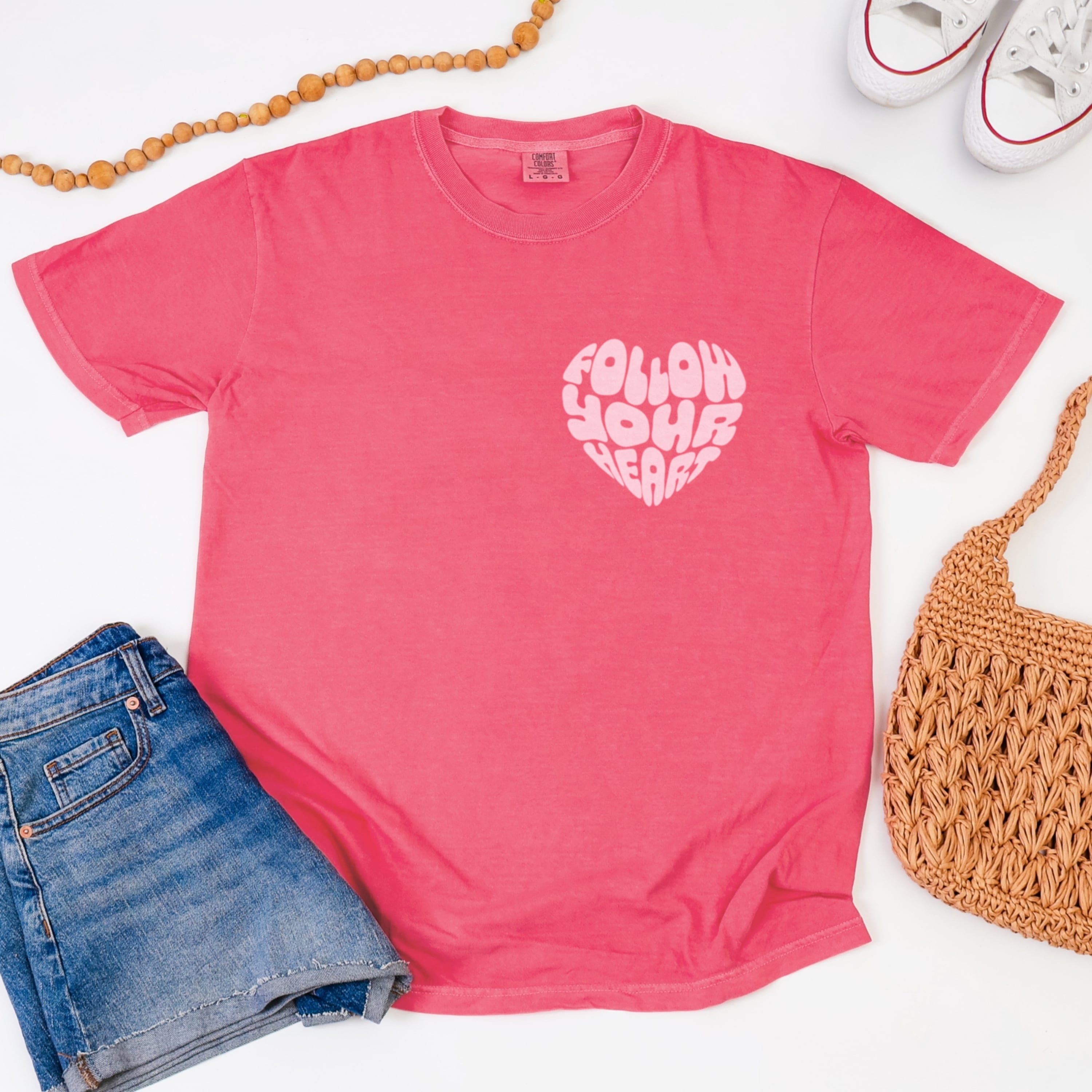 Close up of Follow Your Heart design with heart graphic in light pink on watermelon coral cotton tshirt