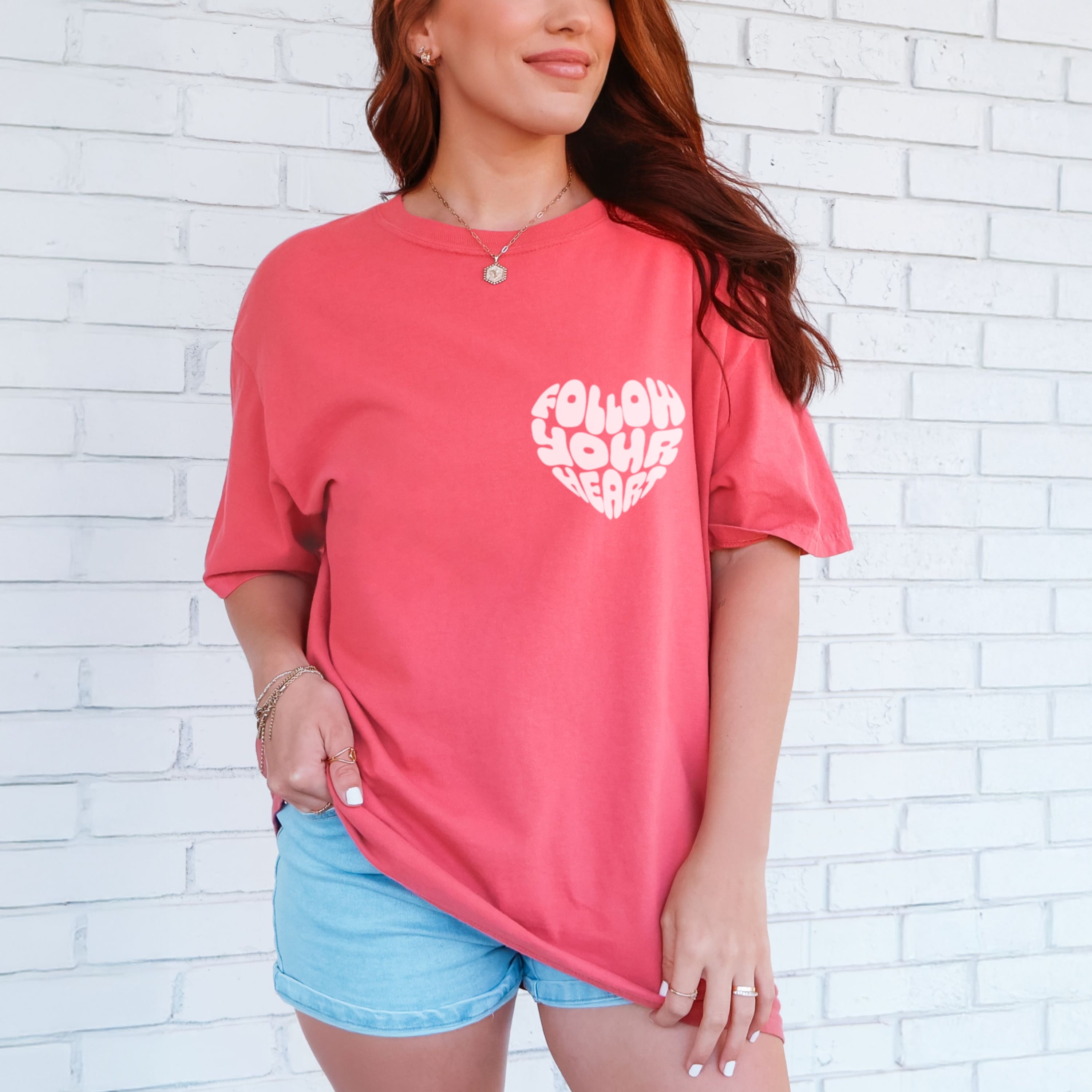 Woman wearing vibrant watermelon Follow Your Heart tshirt with light pink heart design, inspirational graphic tee