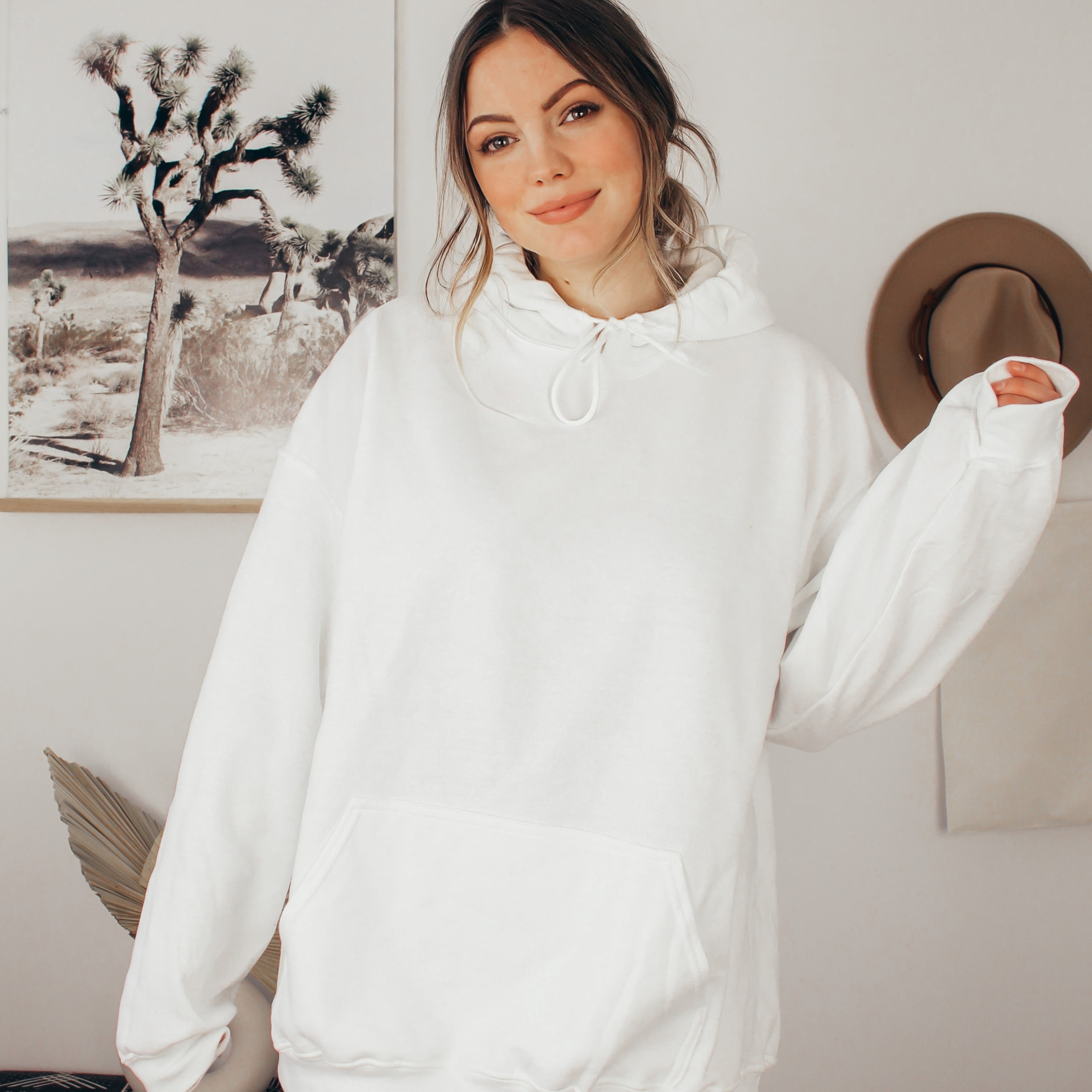 Woman wearing a white hoodie in a room with a framed picture of a desert scene on the wall.