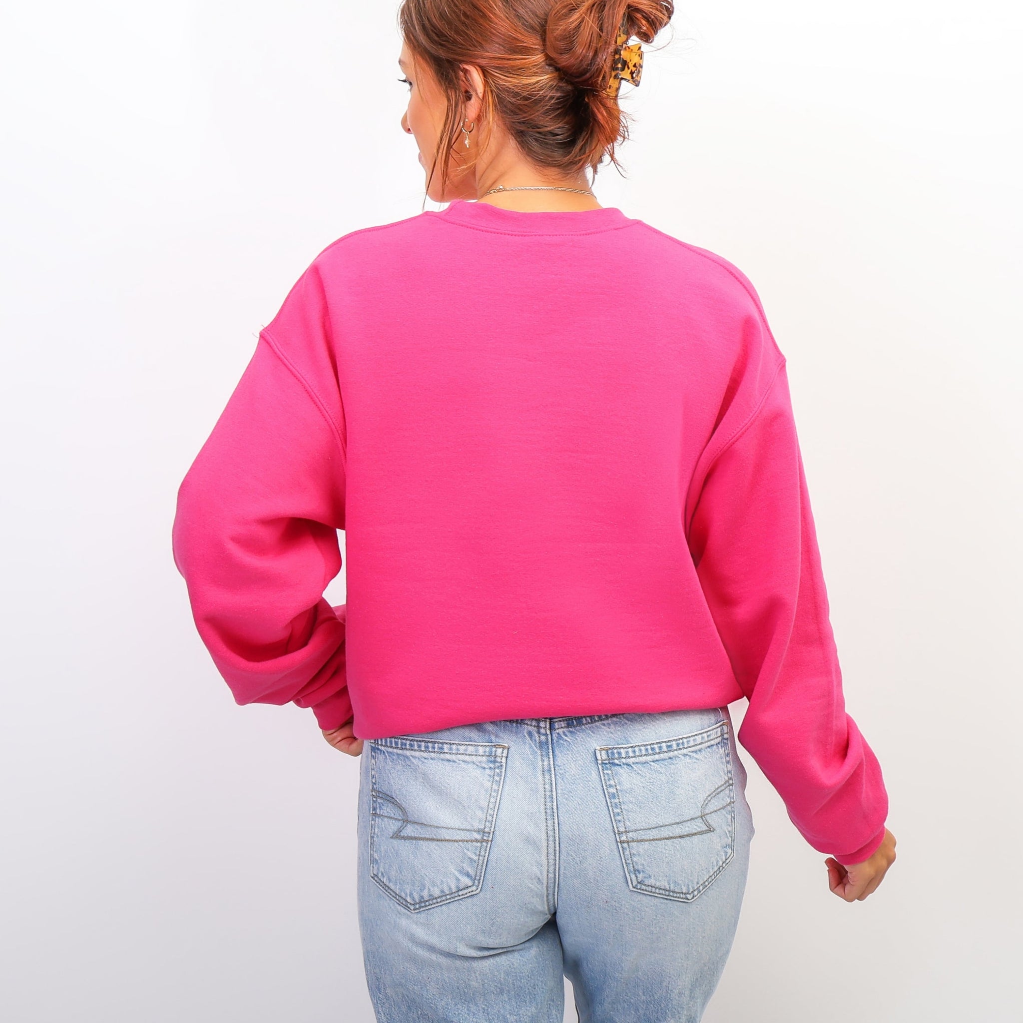 Person wearing a bright pink sweatshirt and light blue jeans on a plain background