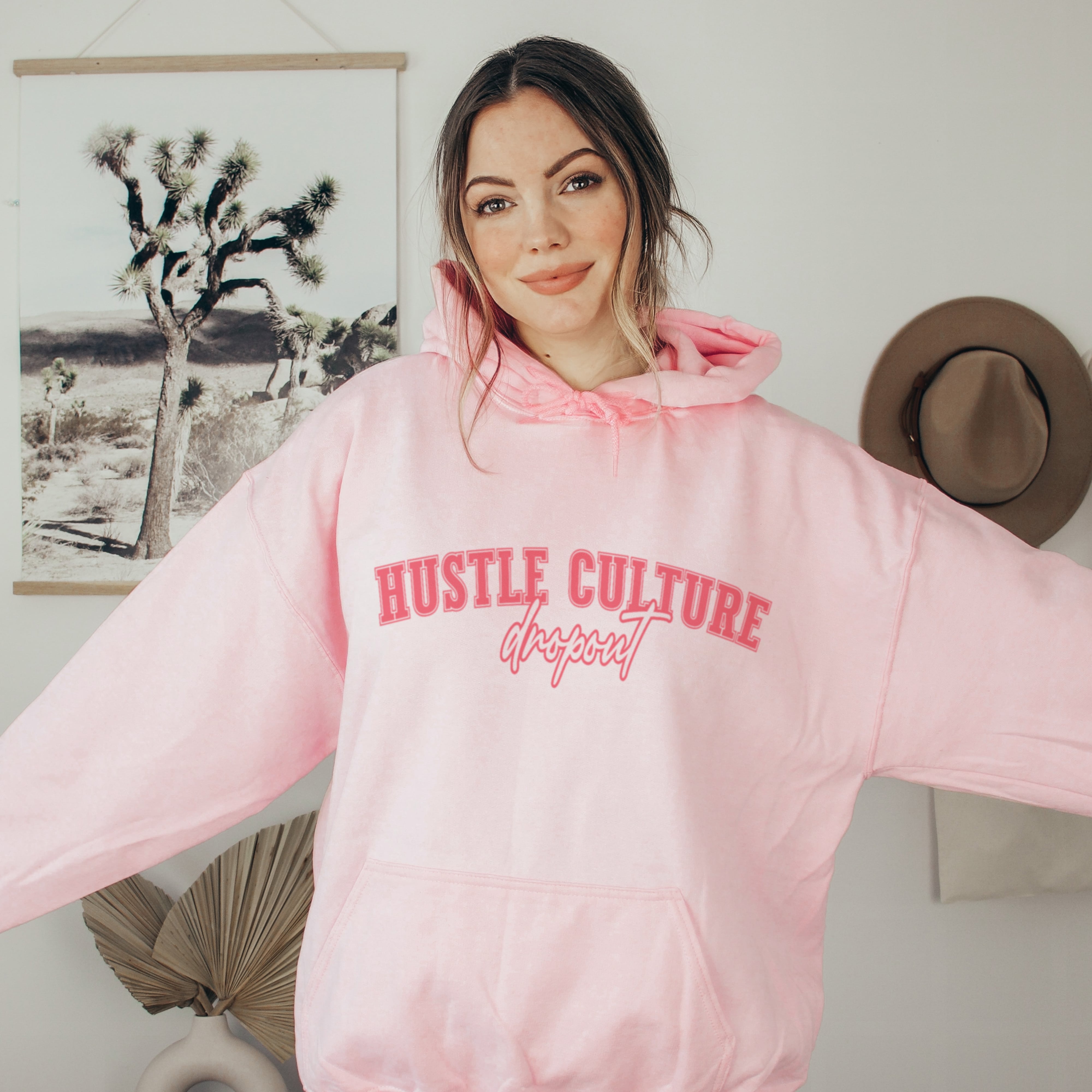 Woman wearing pink hustle culture dropout hoodie, anti-hustle soft life sweatshirt for women