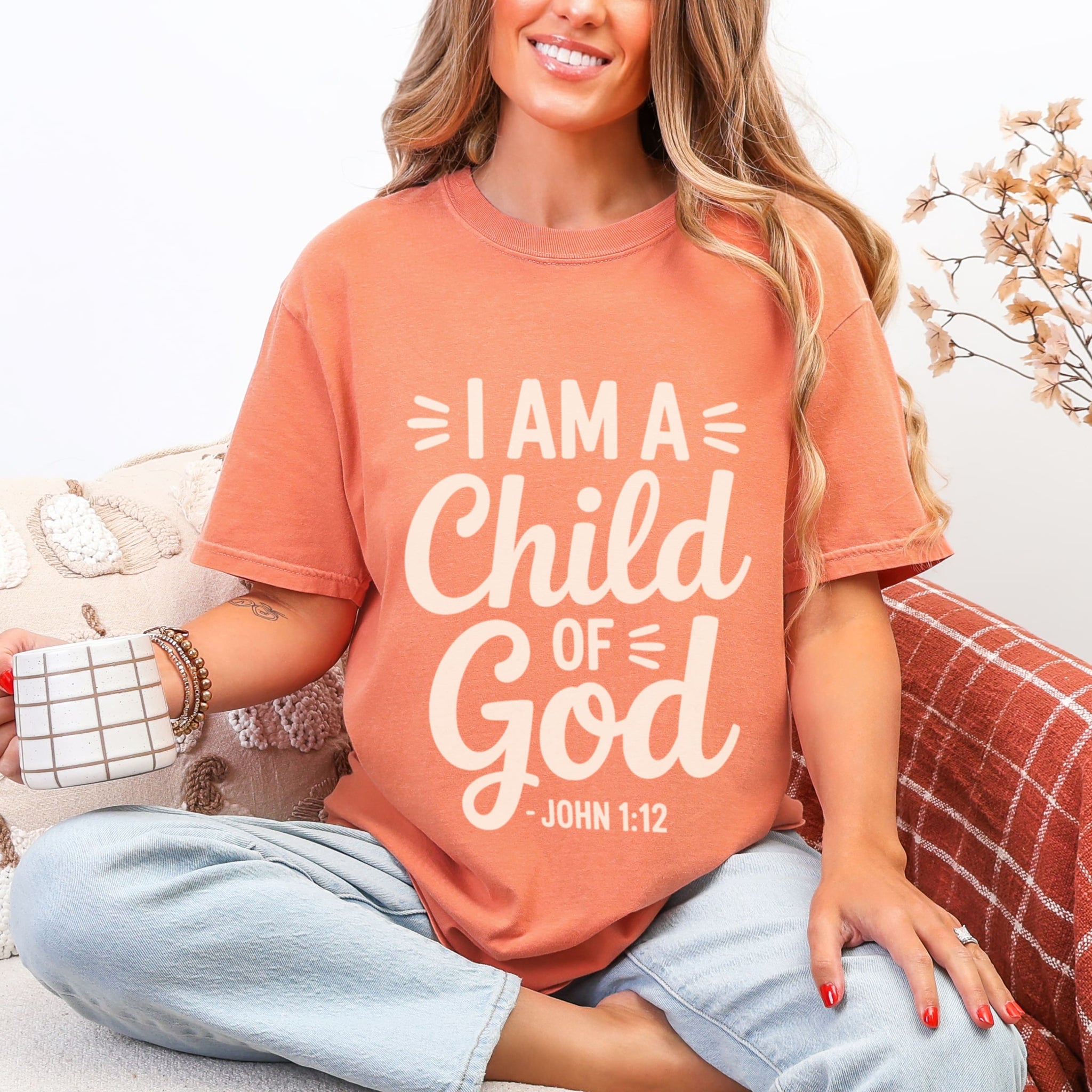 Woman wearing terracotta I Am A Child Of God tshirt with cream lettering and John 1:12, faith-based identity graphic tee