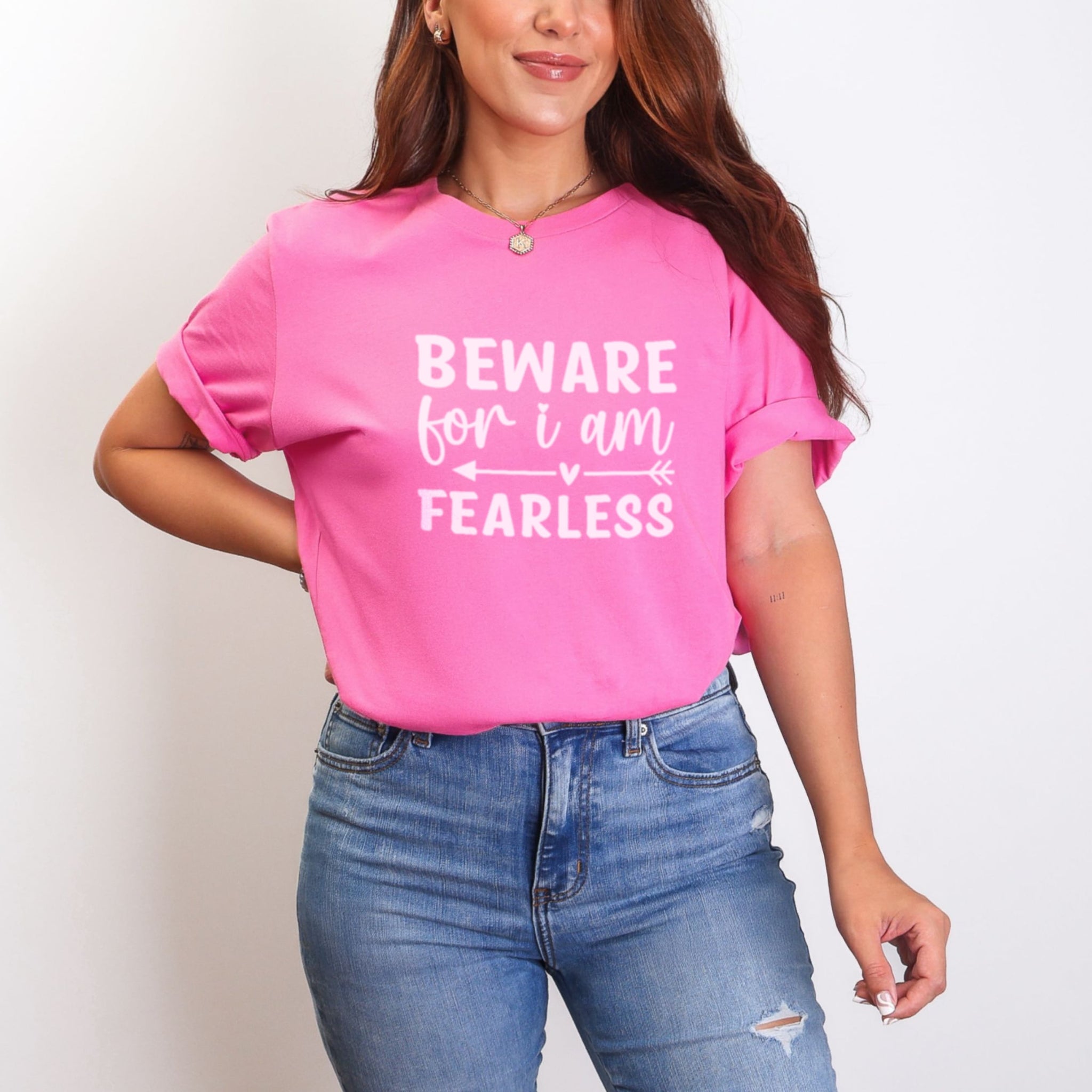 Woman wearing vibrant charity pink Beware For I Am Fearless tshirt with light pink lettering, bold empowerment graphic tee