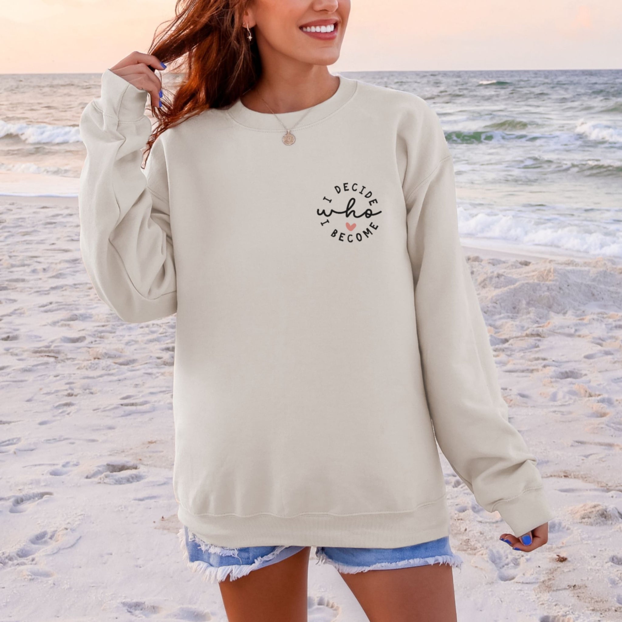 Woman wearing beige I Decide Who I Become chest print sweatshirt at beach - minimalist empowerment crewneck for women