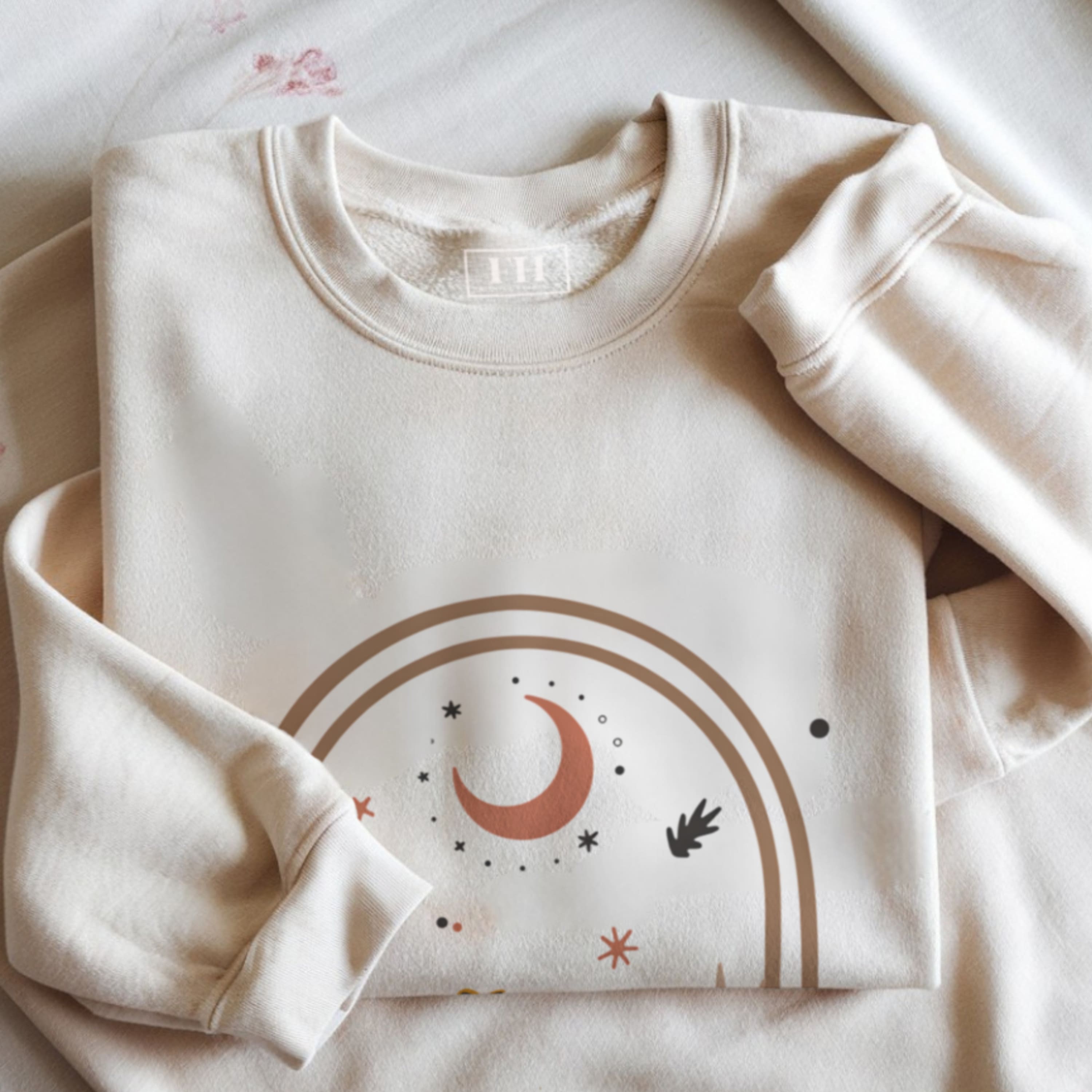 Folded beige sweatshirt with celestial design on a light background