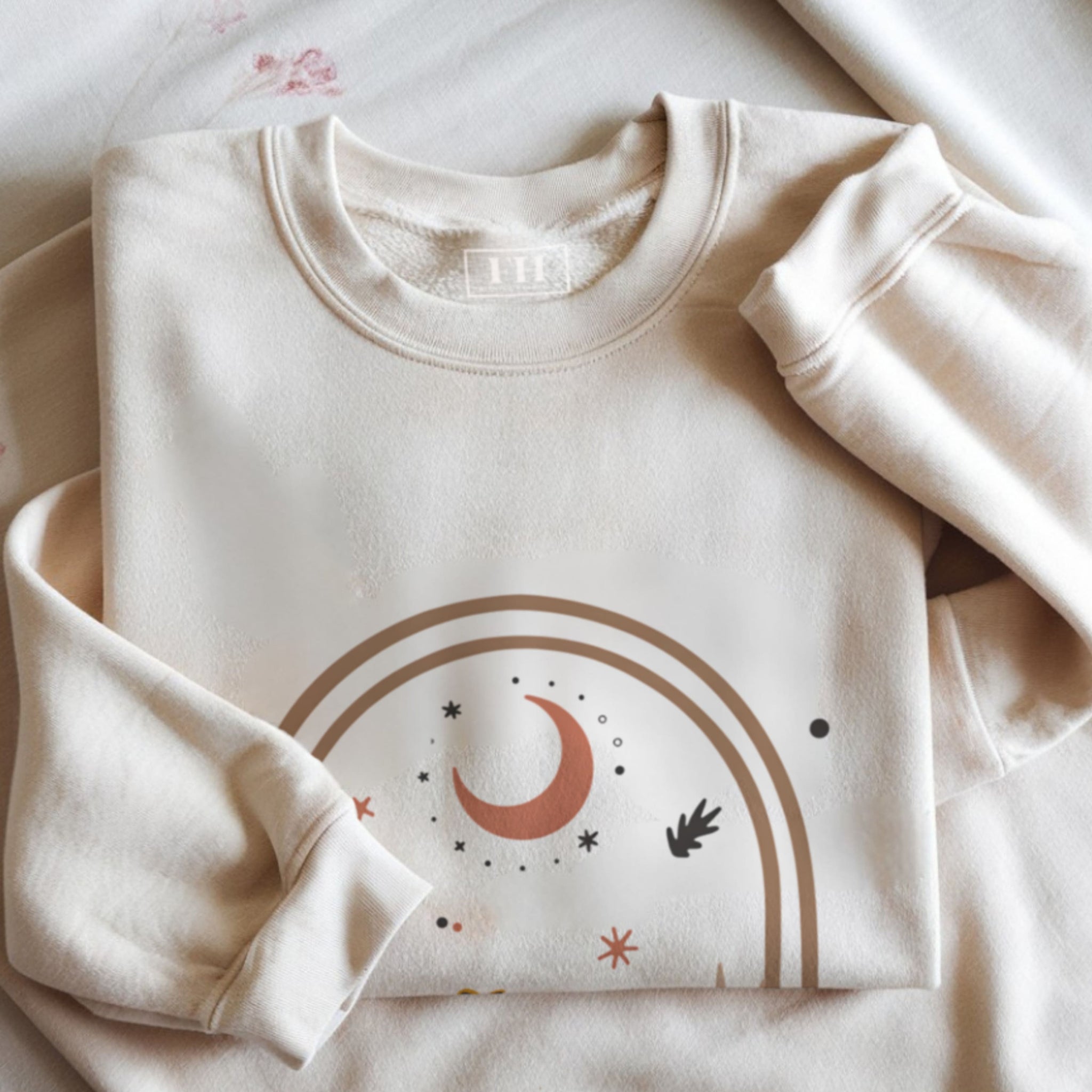Folded beige sweatshirt with celestial design on a light background