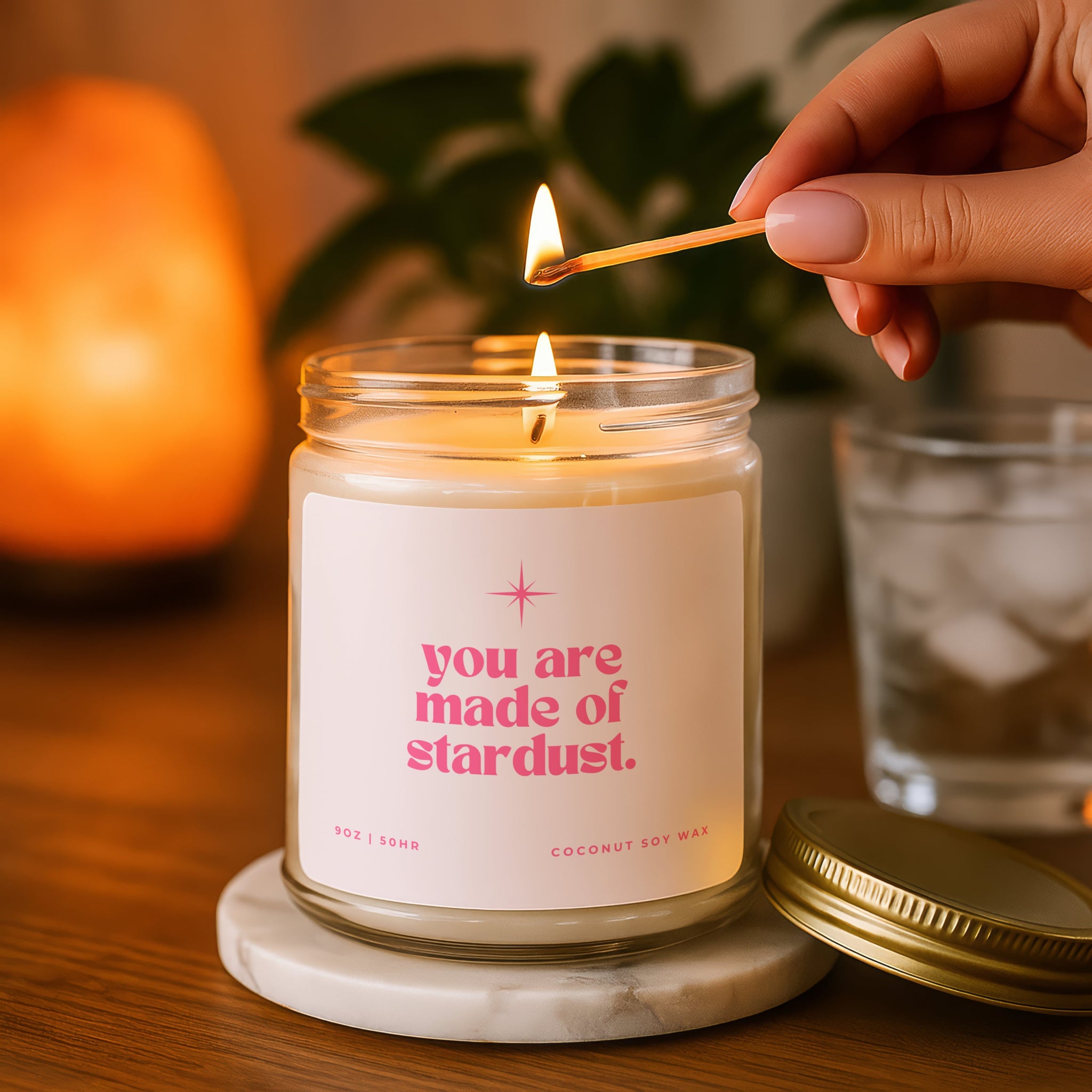 Candle being lit with a match, featuring a label 'you are made of stardust' on a wooden surface.