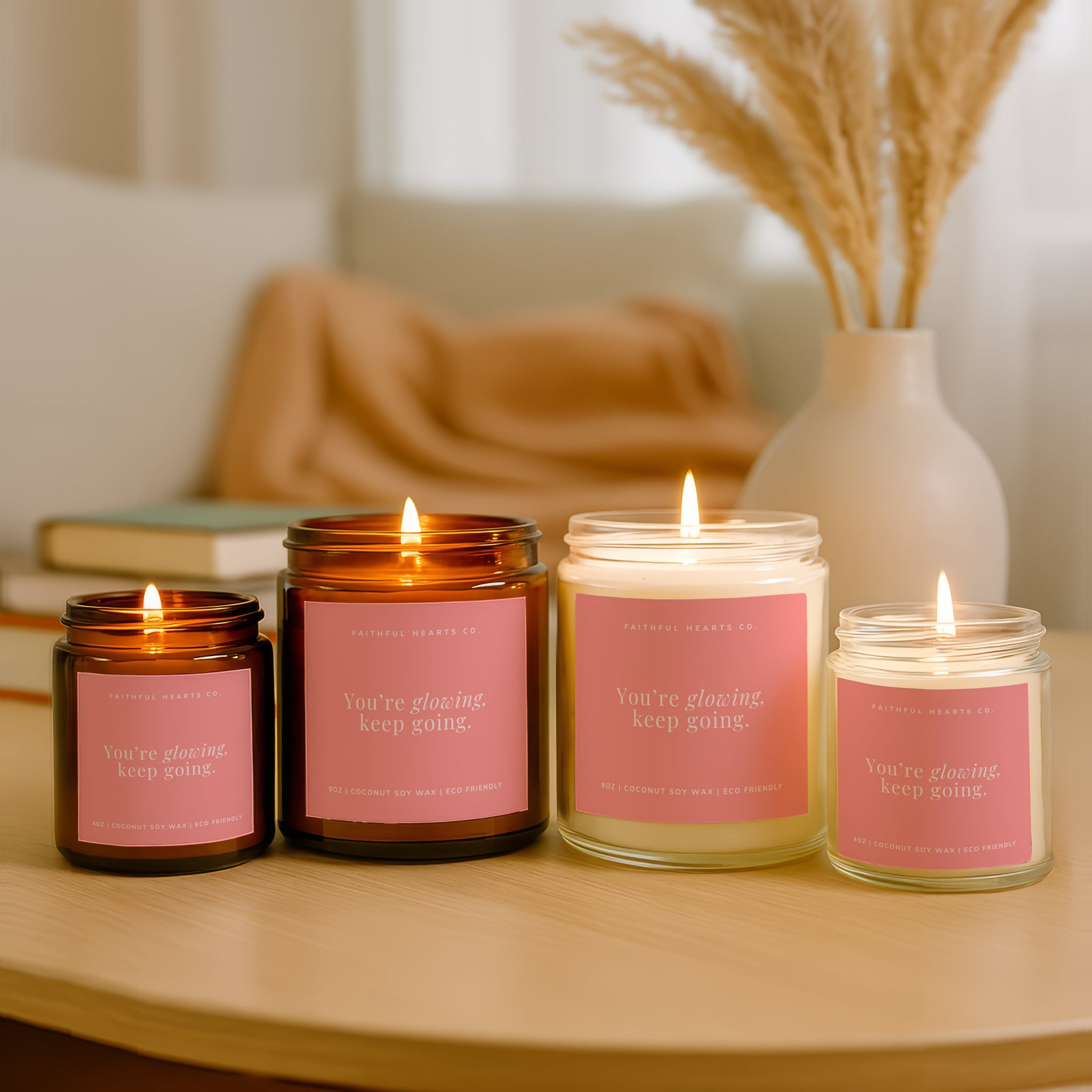 Four lit candle gifts with pink labels on a wooden surface, with a vase and books in the background.