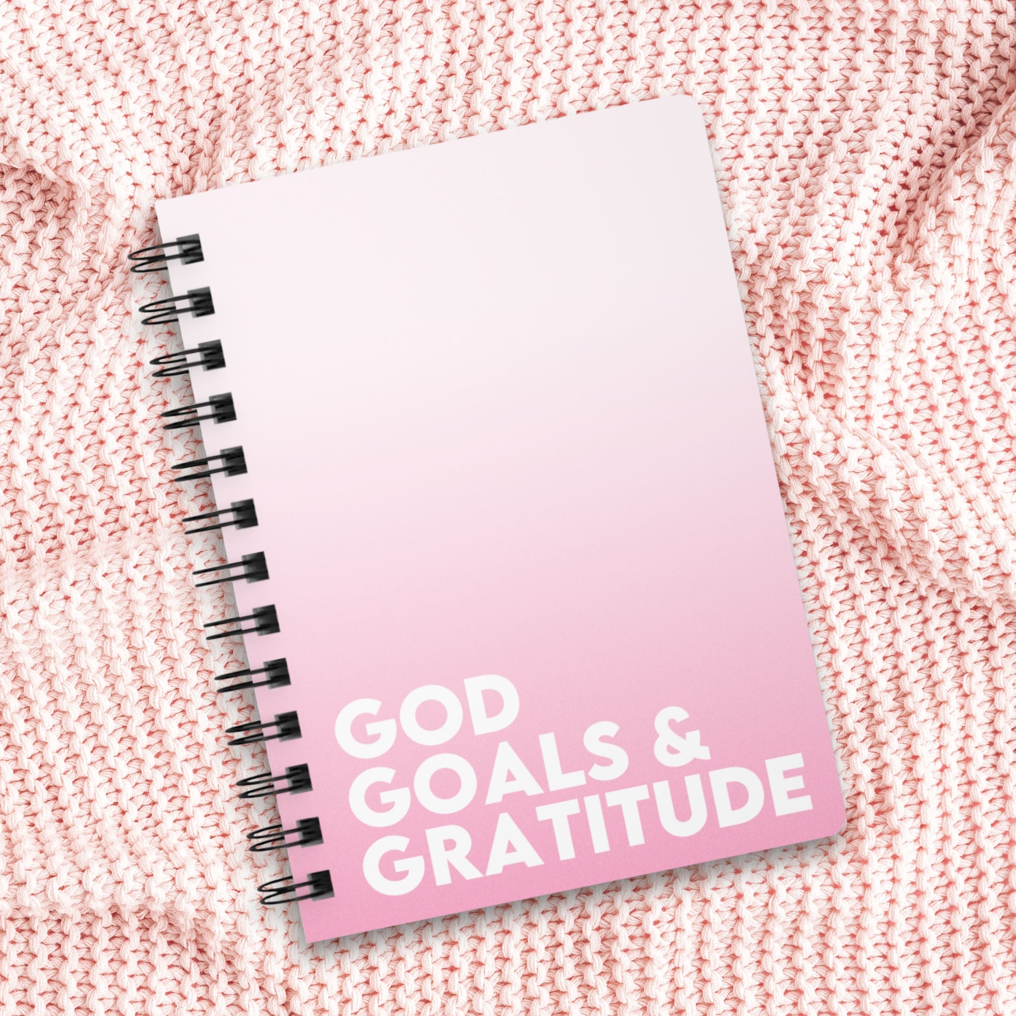 Pink ombre notebook with 'GOD GOALS & GRATITUDE' text on a textured pink surface