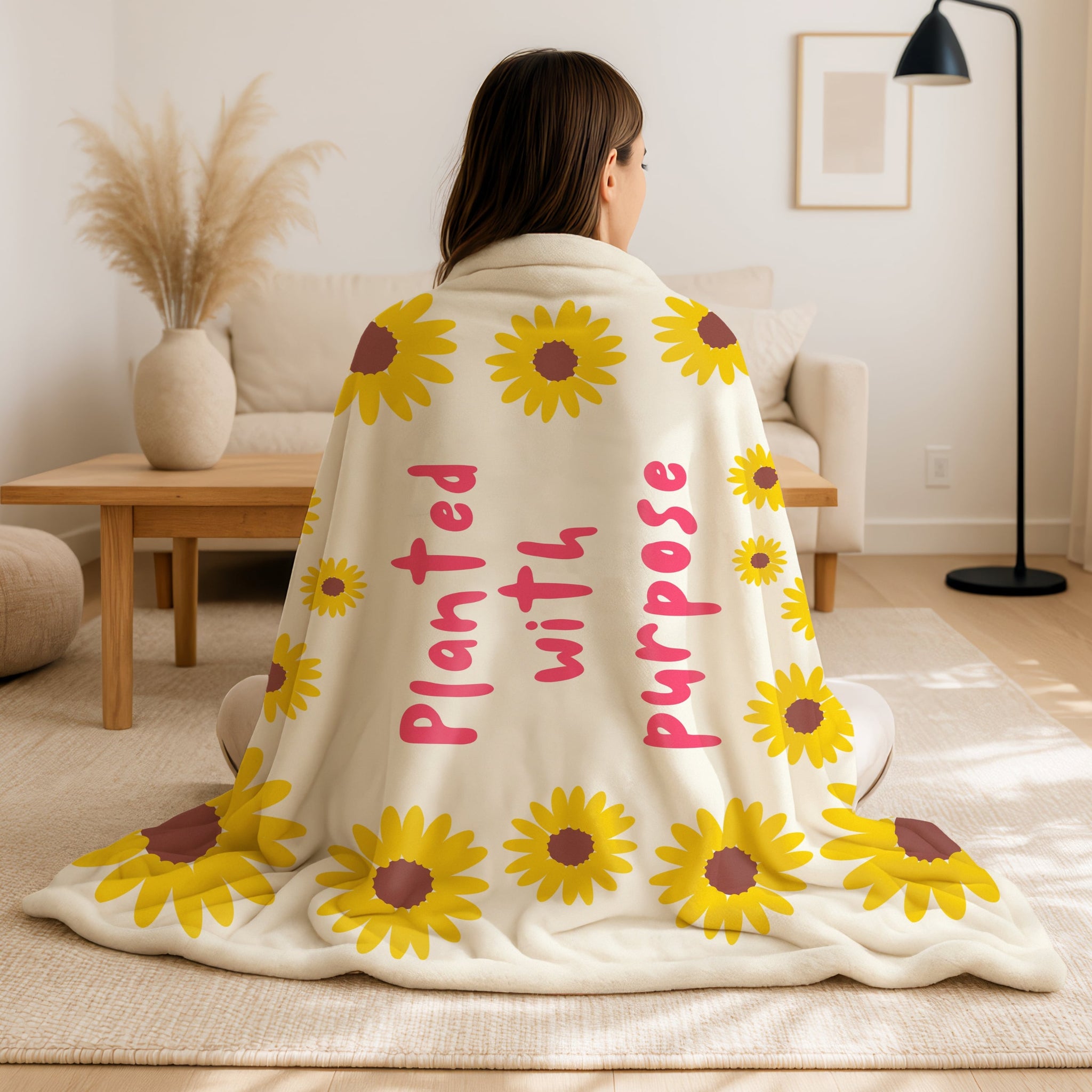 Person wrapped in a blanket with sunflower patterns and text in a living room.