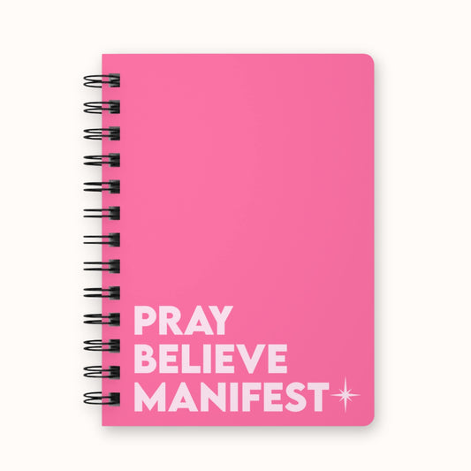 Pink spiral notebook with 'Pray Believe Manifest' text and star detail on front cover