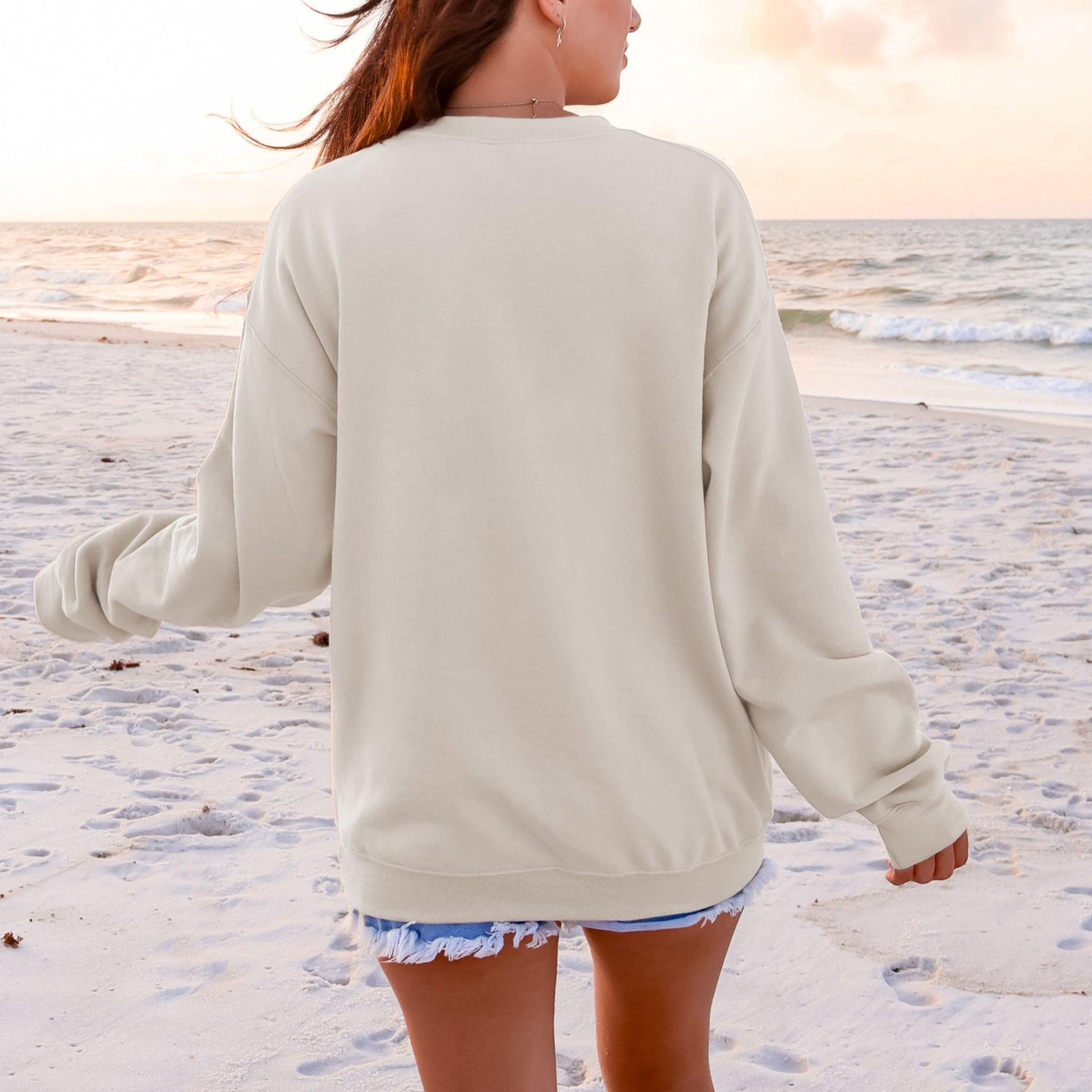 Back view of beige God Works For The Good sweatshirt at beach - oversized Christian Romans 8:28 crewneck for women