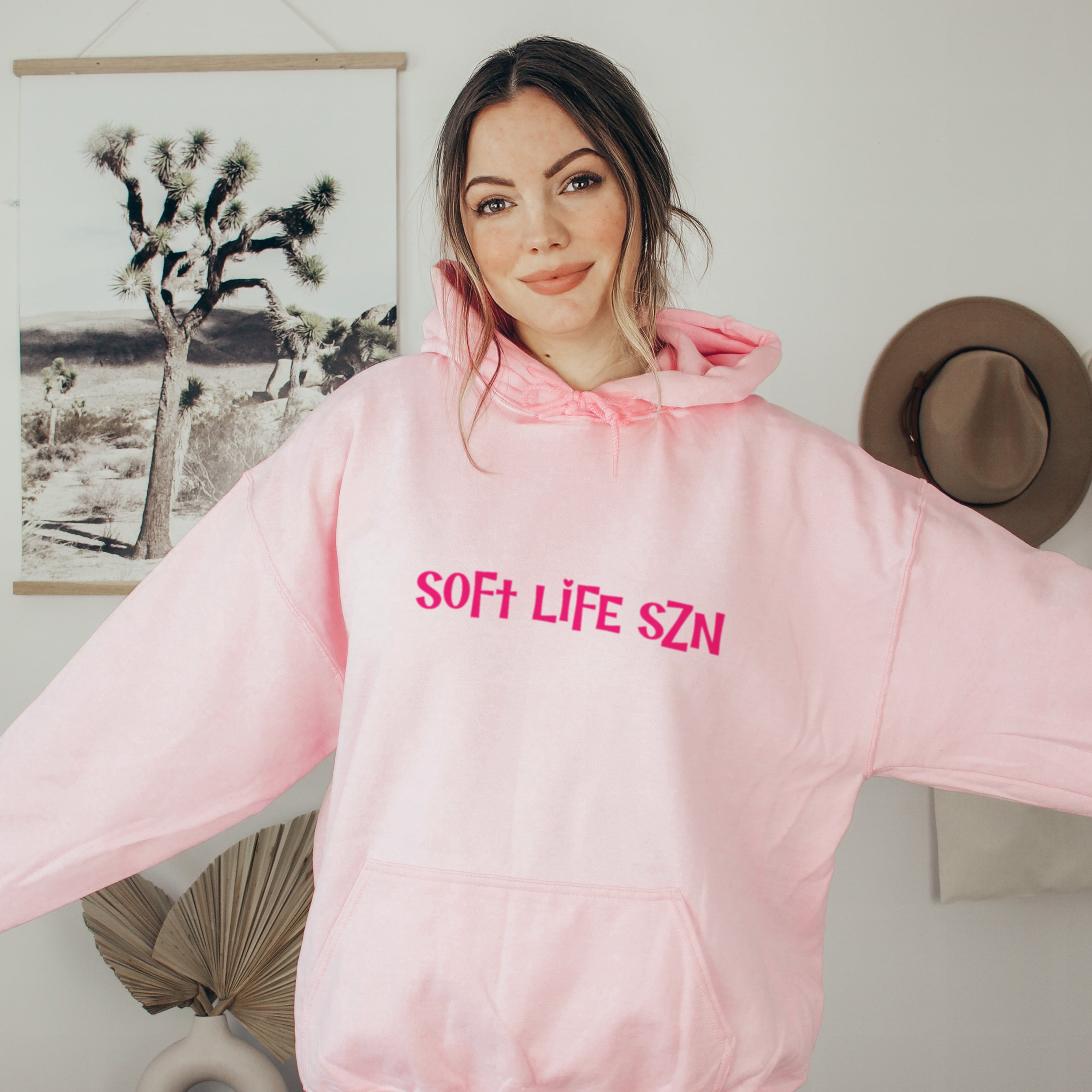 Person wearing a pink hoodie with 'SOFT LIFE SZN' text, for soft girl era