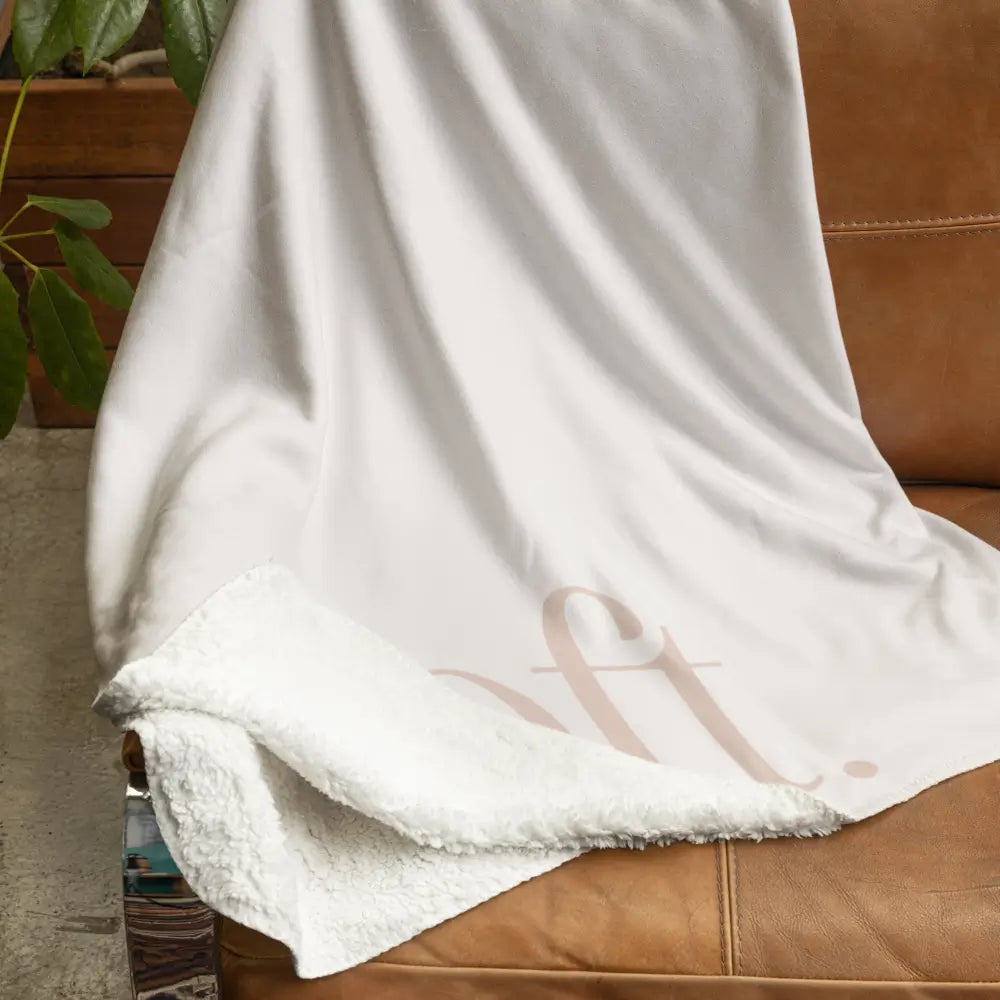 luxury sherpa fleece blanket from Faithful Hearts in cream with the word soft on the front draped over a chair