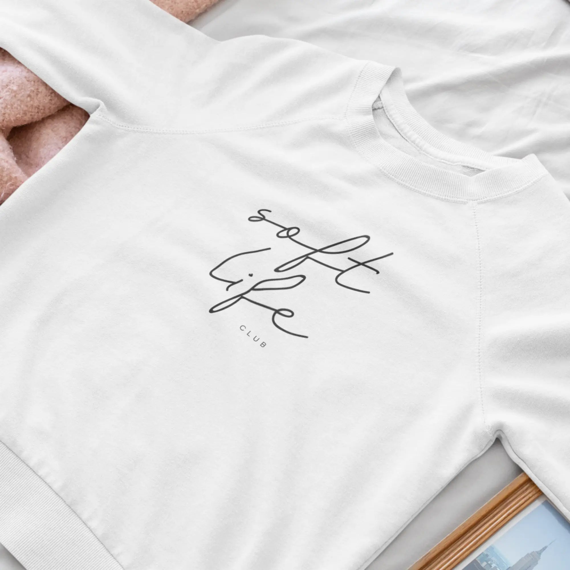 Flat lay sweatshirt for women in white with Soft Life Club text across the front in a black signature font