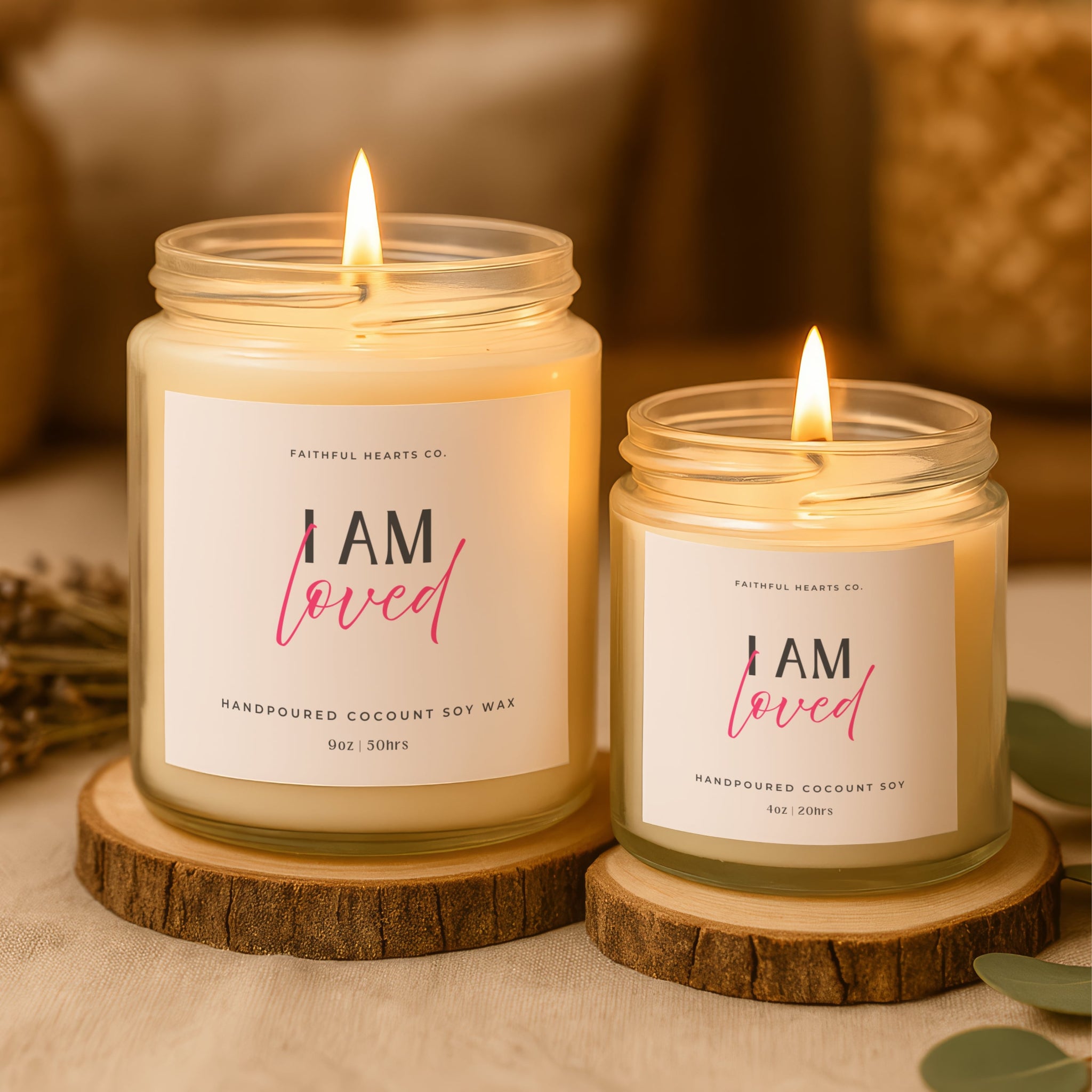 Two candles with 'I AM loved' labels on wooden stands against a blurred background