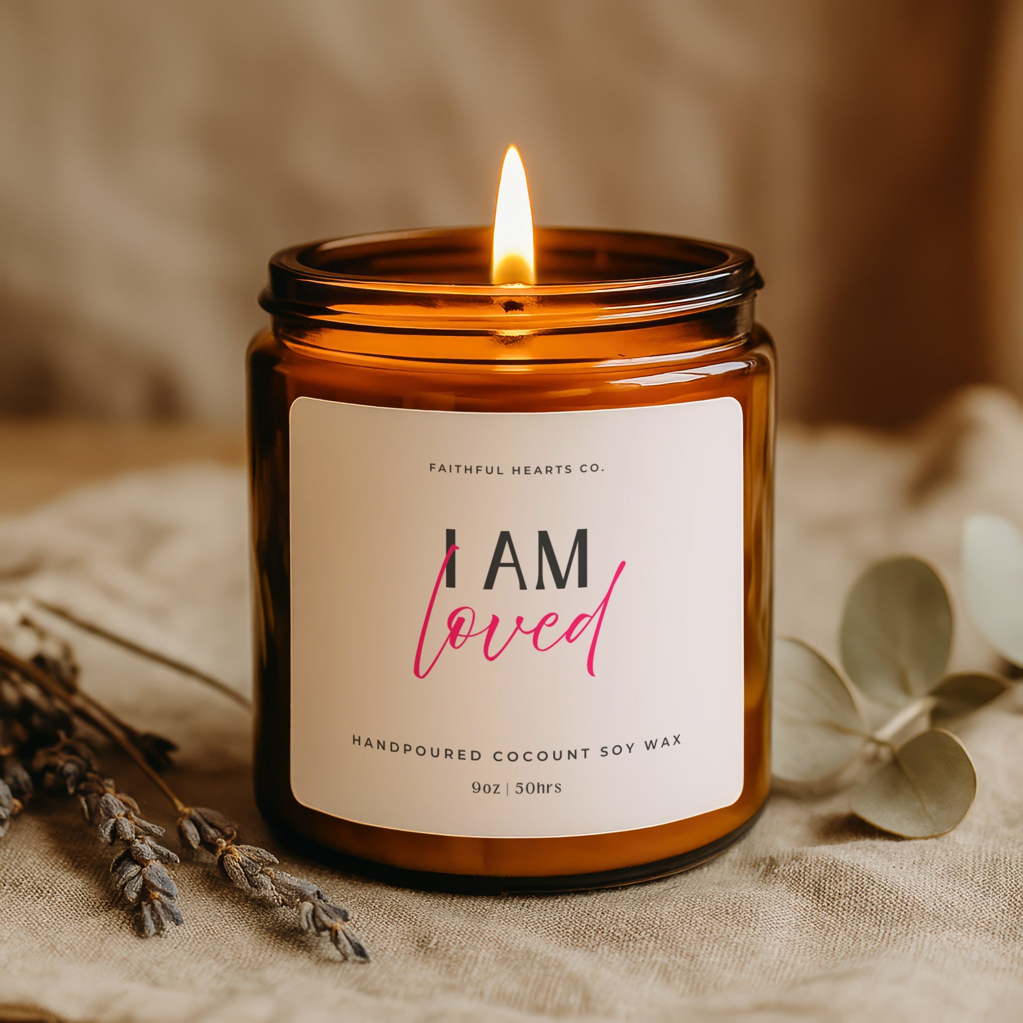 Candle in an amber jar with a 'I AM loved' label on a textured surface.