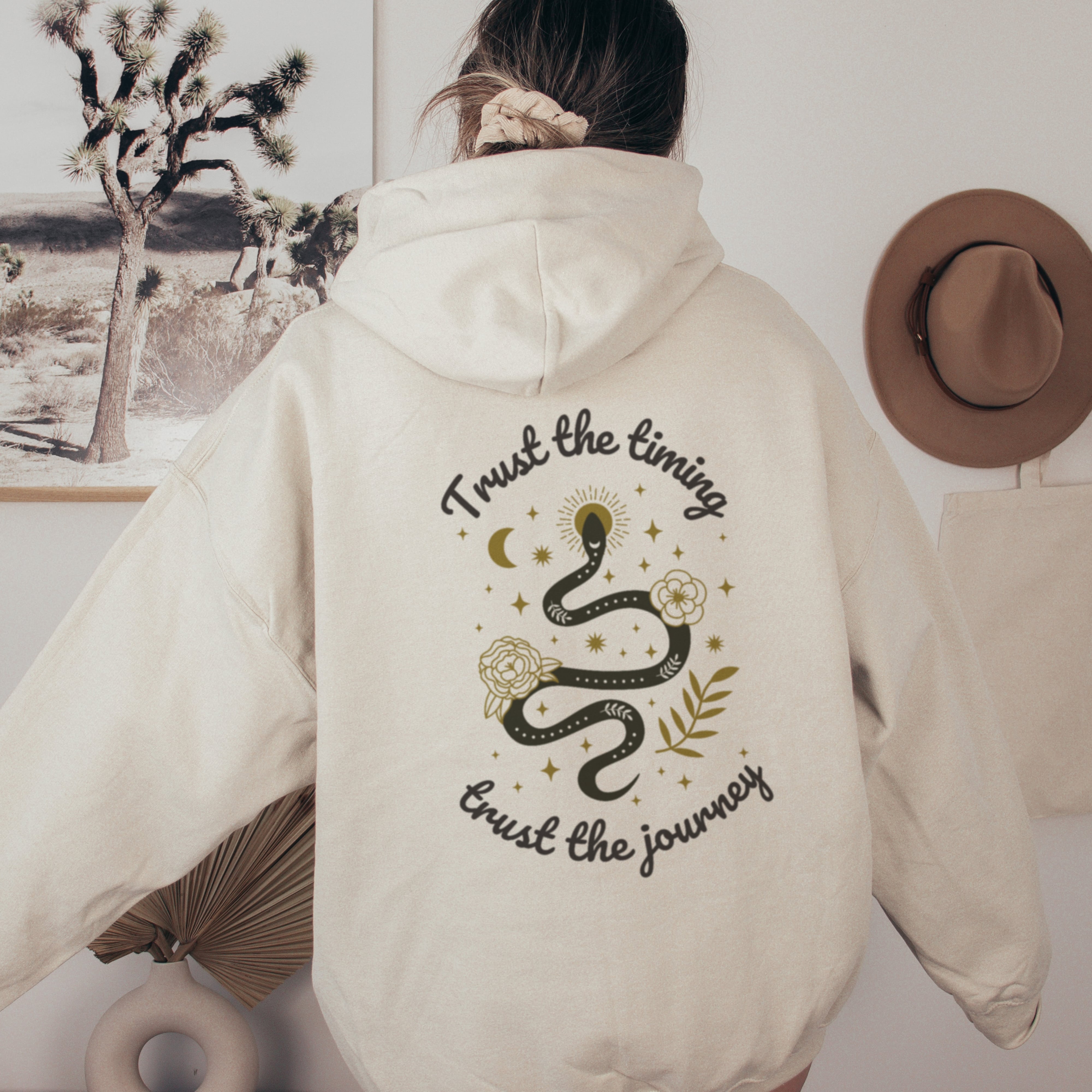 Person wearing a beige hoodie with a snake design and text on the back, standing in a desert-themed room.