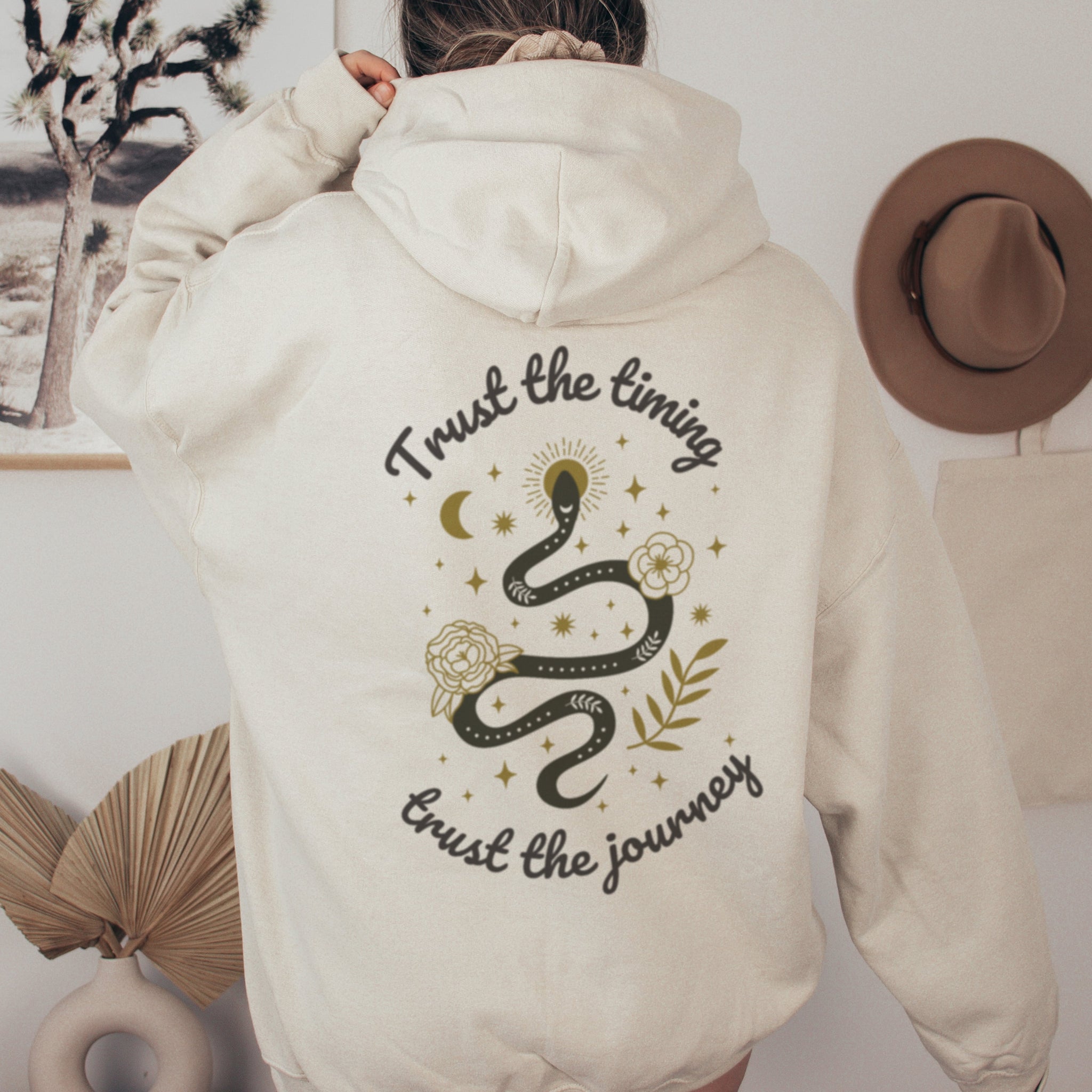 Back of beige spiritual hoodie with trust the timing trust the journey text and celestial snake design with moons stars and flowers
