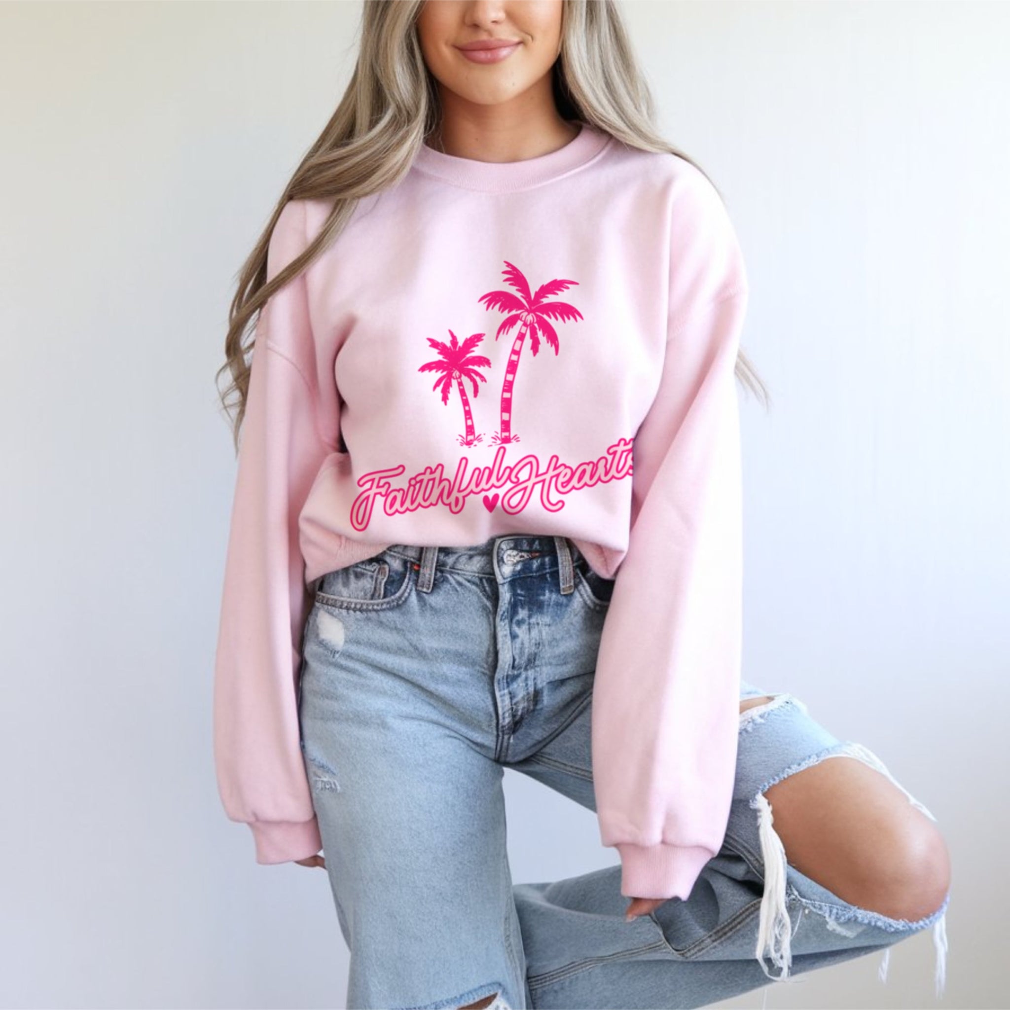 Woman wearing Faithful Hearts pale pink crewneck sweatshirt with jeans, coastal Christian aesthetic fashion for women