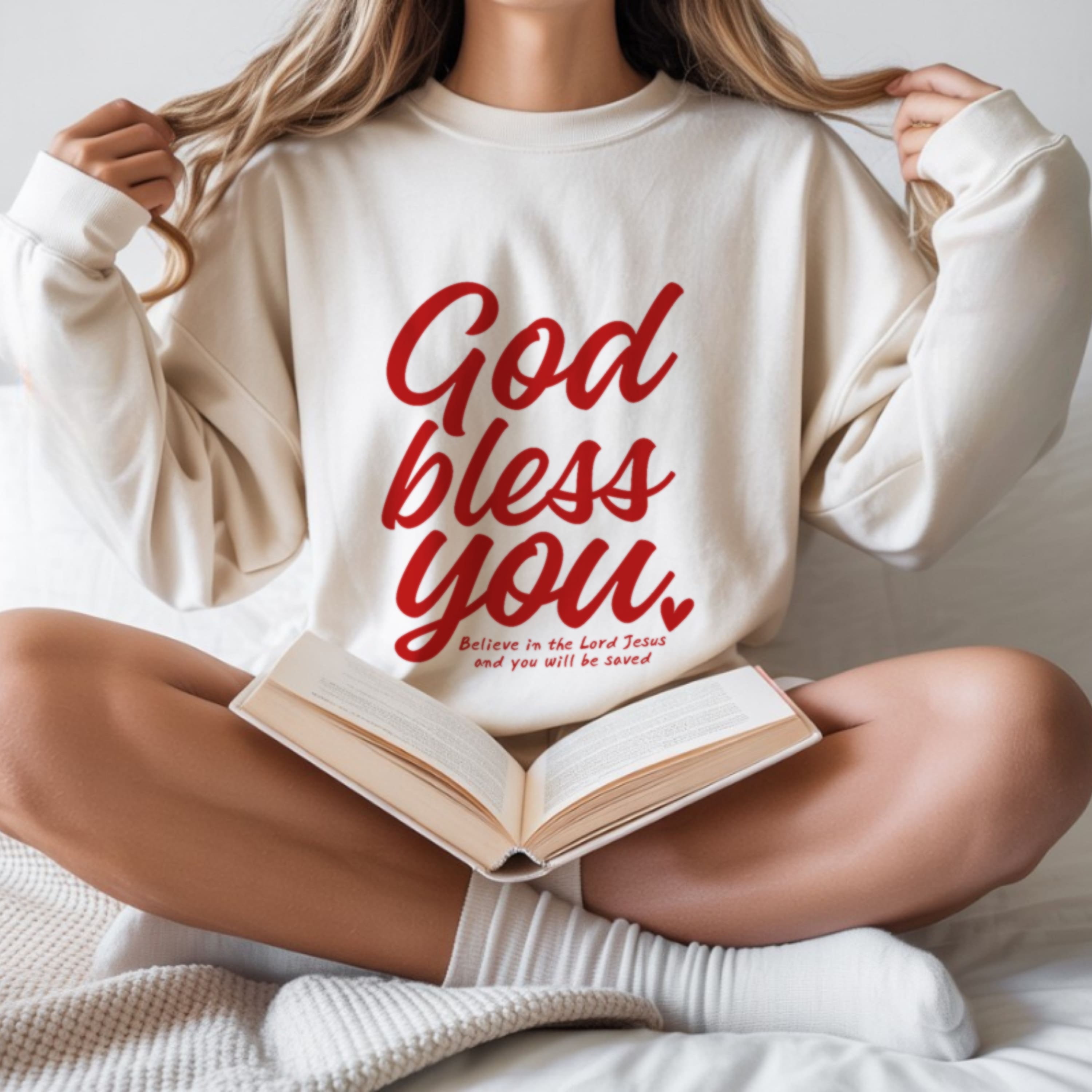 Woman wearing God Bless You white crewneck sweatshirt reading Bible, scripture based Christian fashion for women