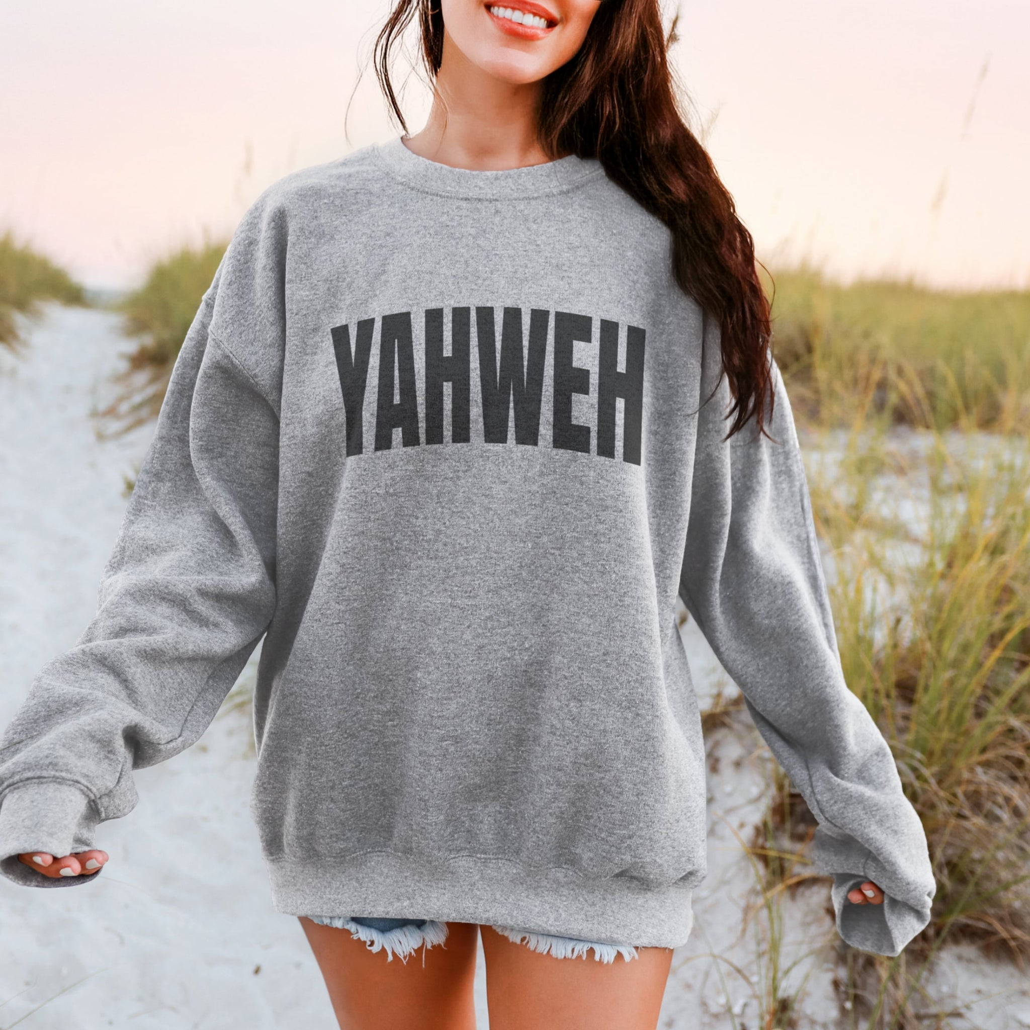 Woman wearing oversized grey YAHWEH sweatshirt outdoors - bold Christian Hebrew name of God crewneck for women