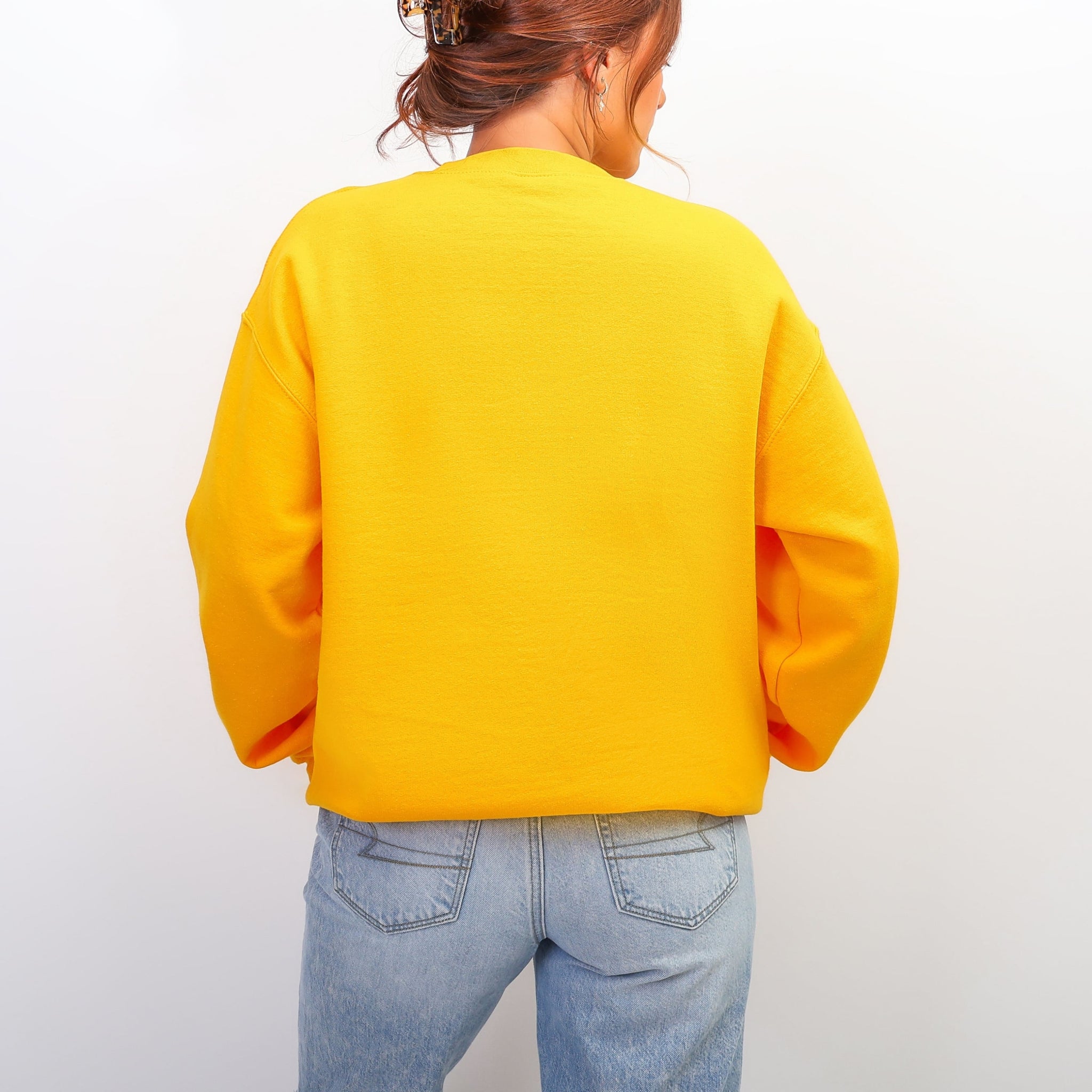 Back of yellow Love Never Fails sweatshirt with 1 Corinthians 13:8 message