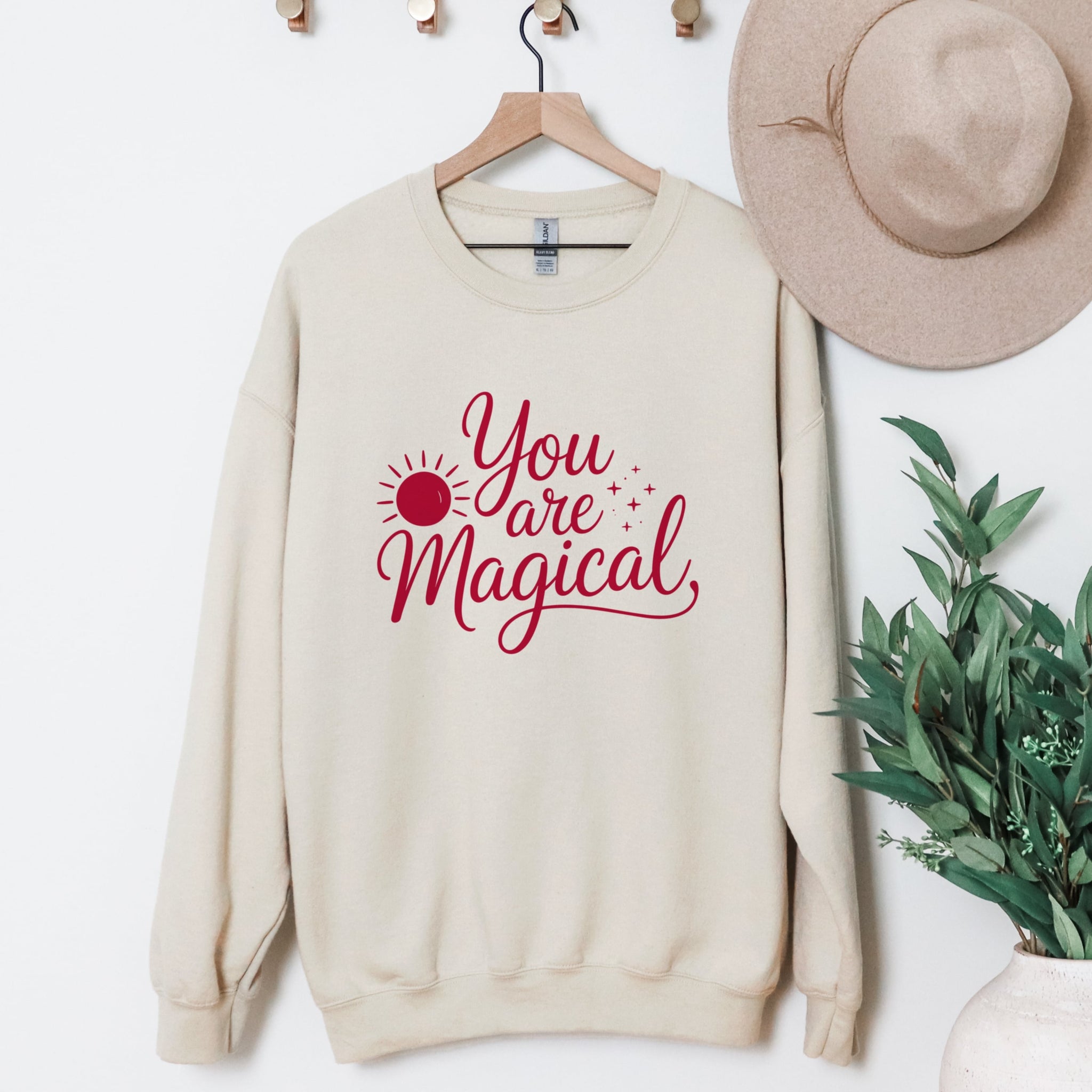 Cream You Are Magical sweatshirt with sun detail in red on a coat hanger.