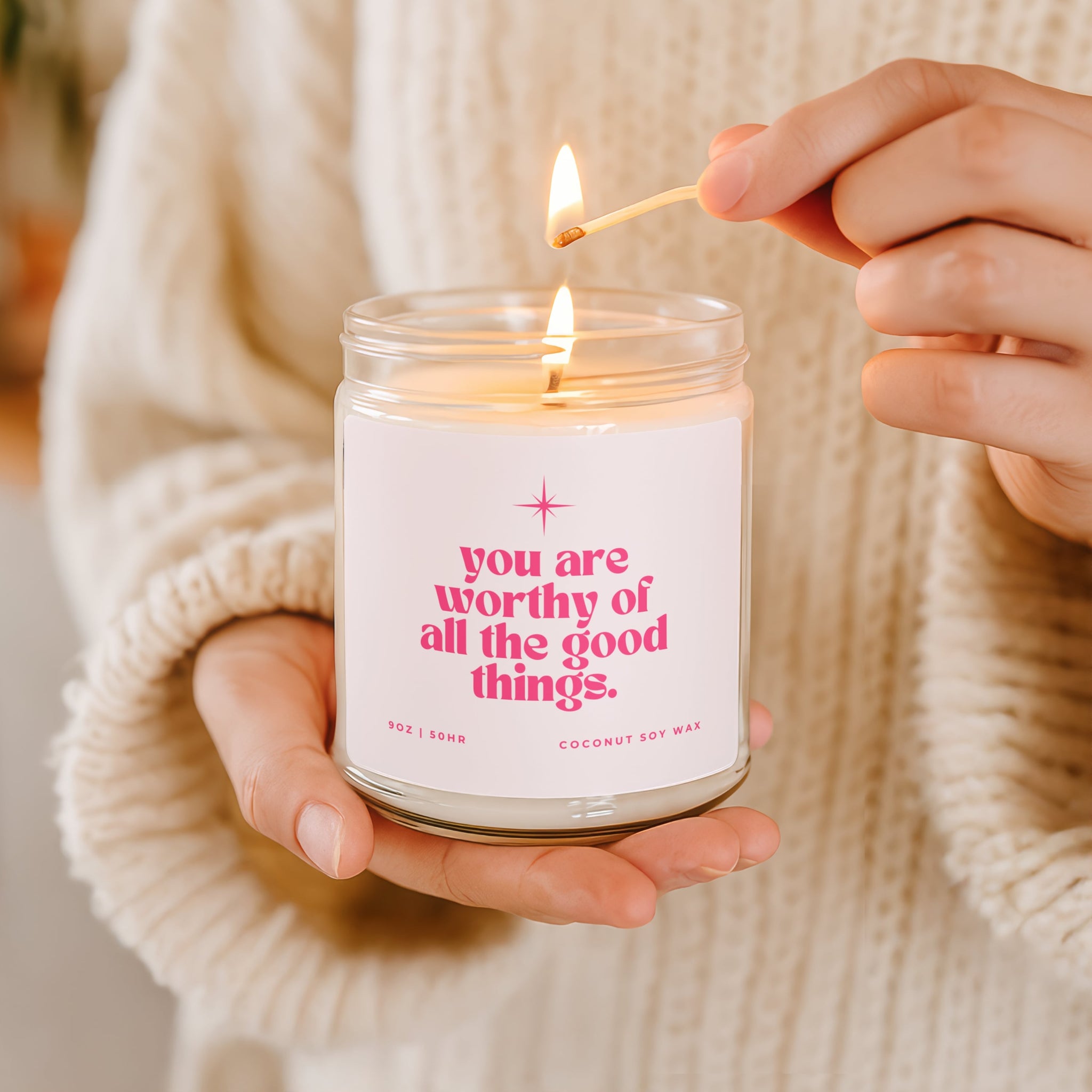 Candle with motivational message being lit by a person wearing a beige sweater.